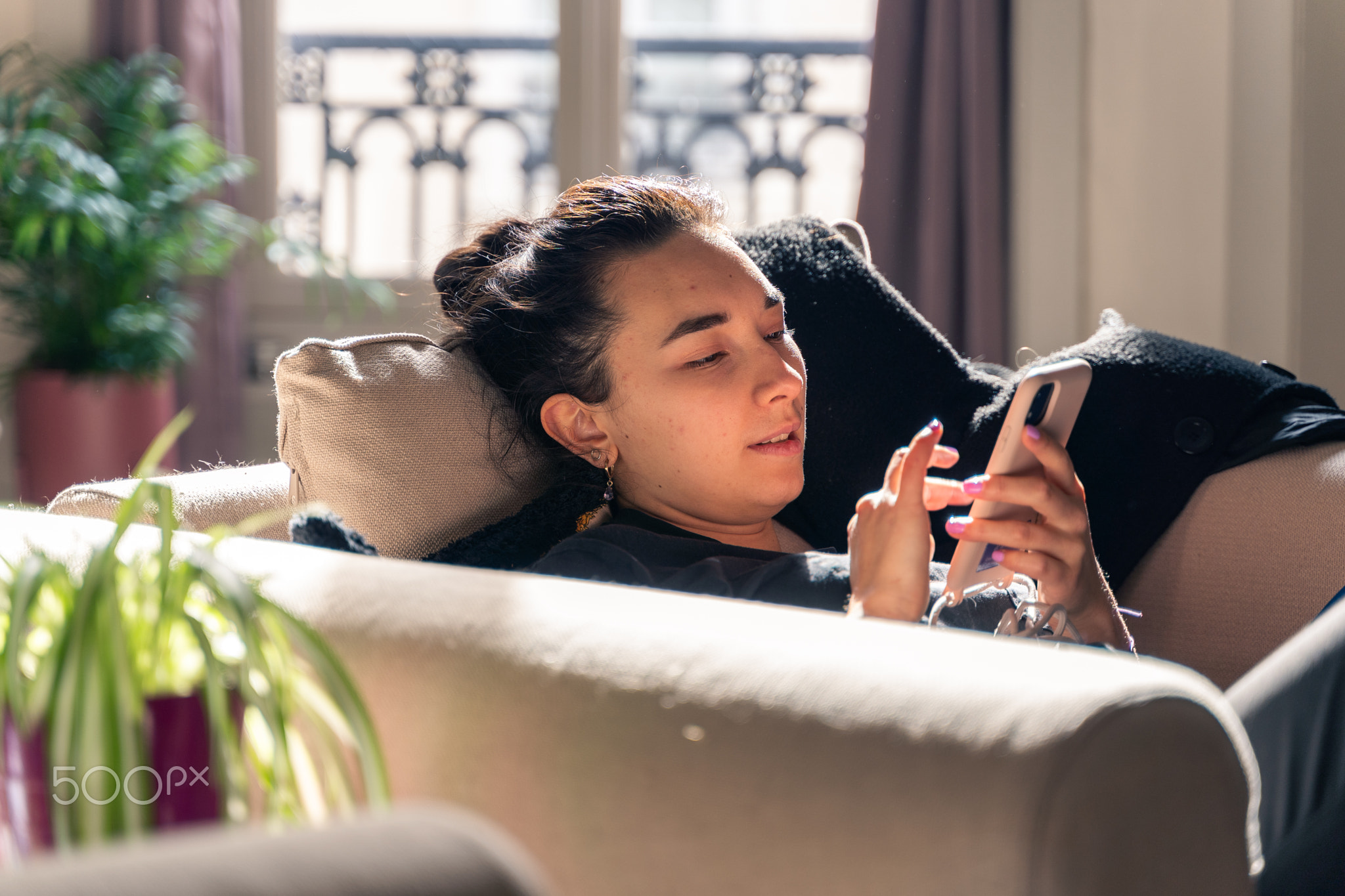Relaxed young Asian woman on her sofa with her smartphone at home