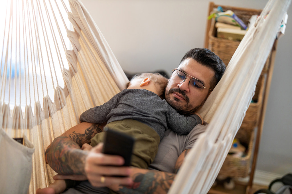 Man checking his phone while his little baby son is sleeping by Edyta Pawlowska on 500px.com