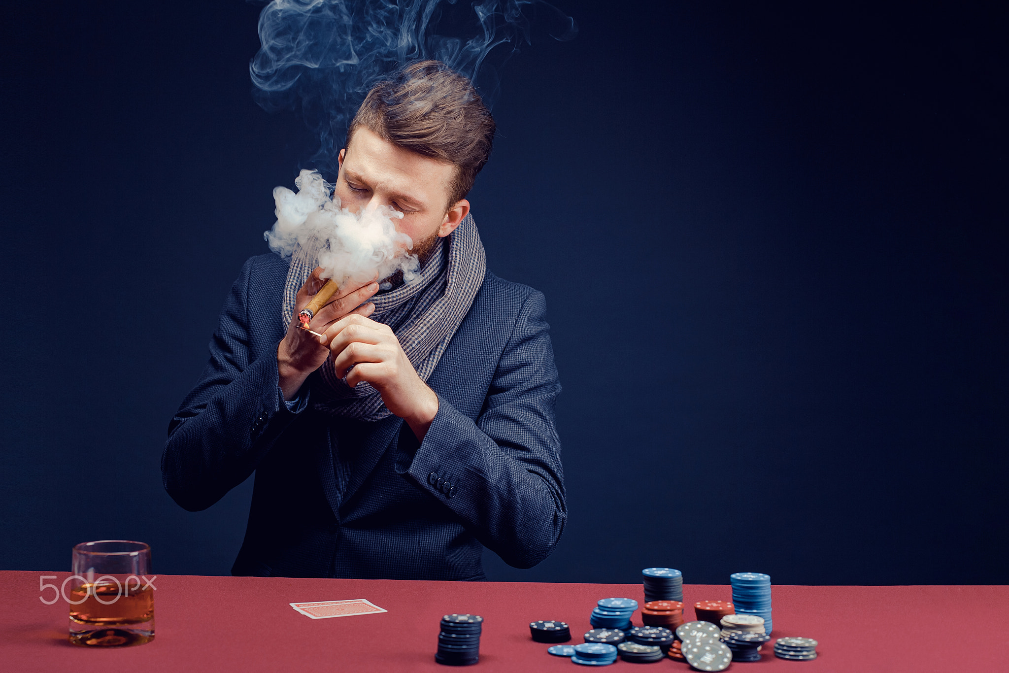 Stylish bearded Man in suit and scarf playing in dark casino, smoking