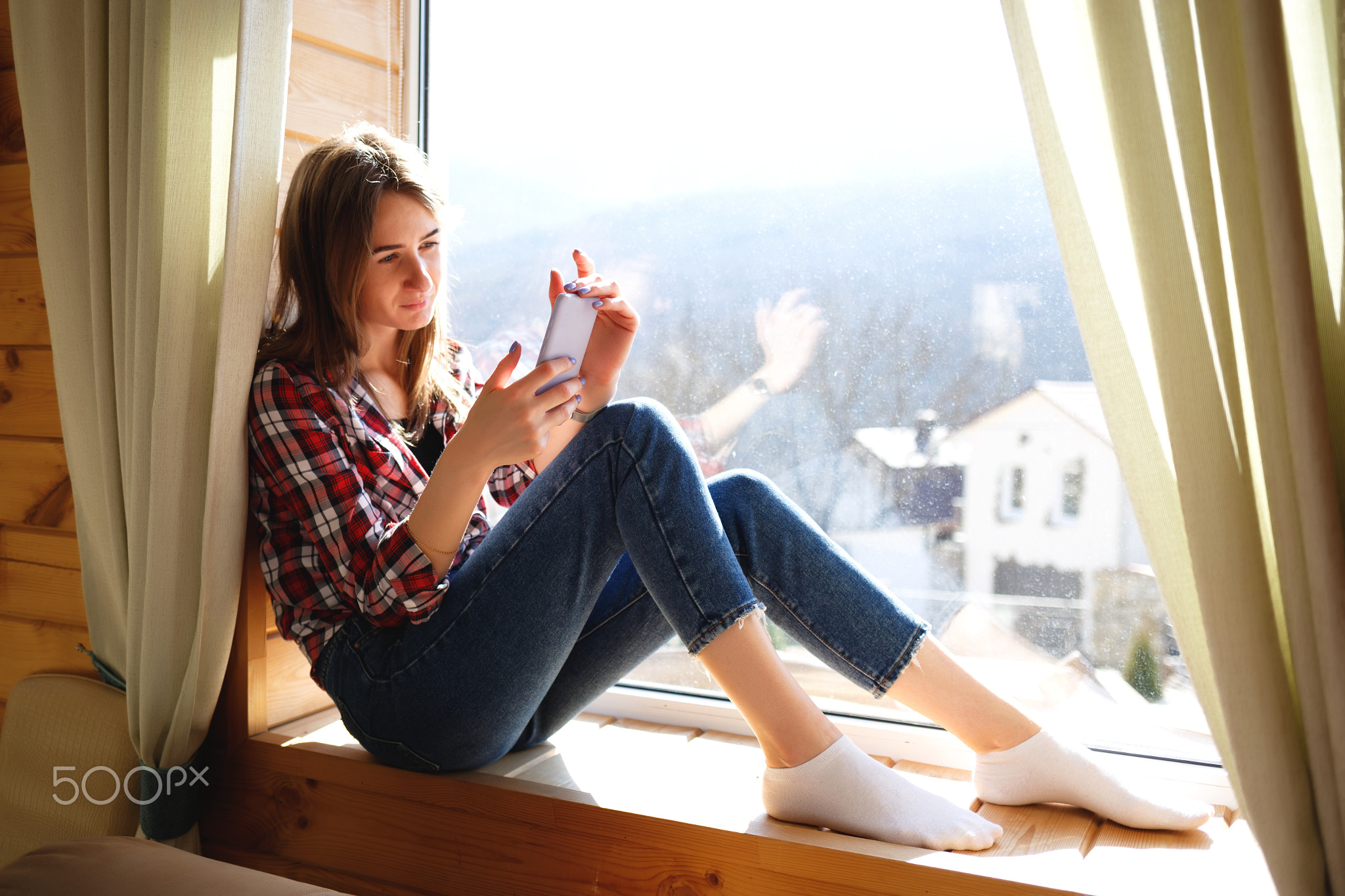 young girl talking on the phone while sitting by the window