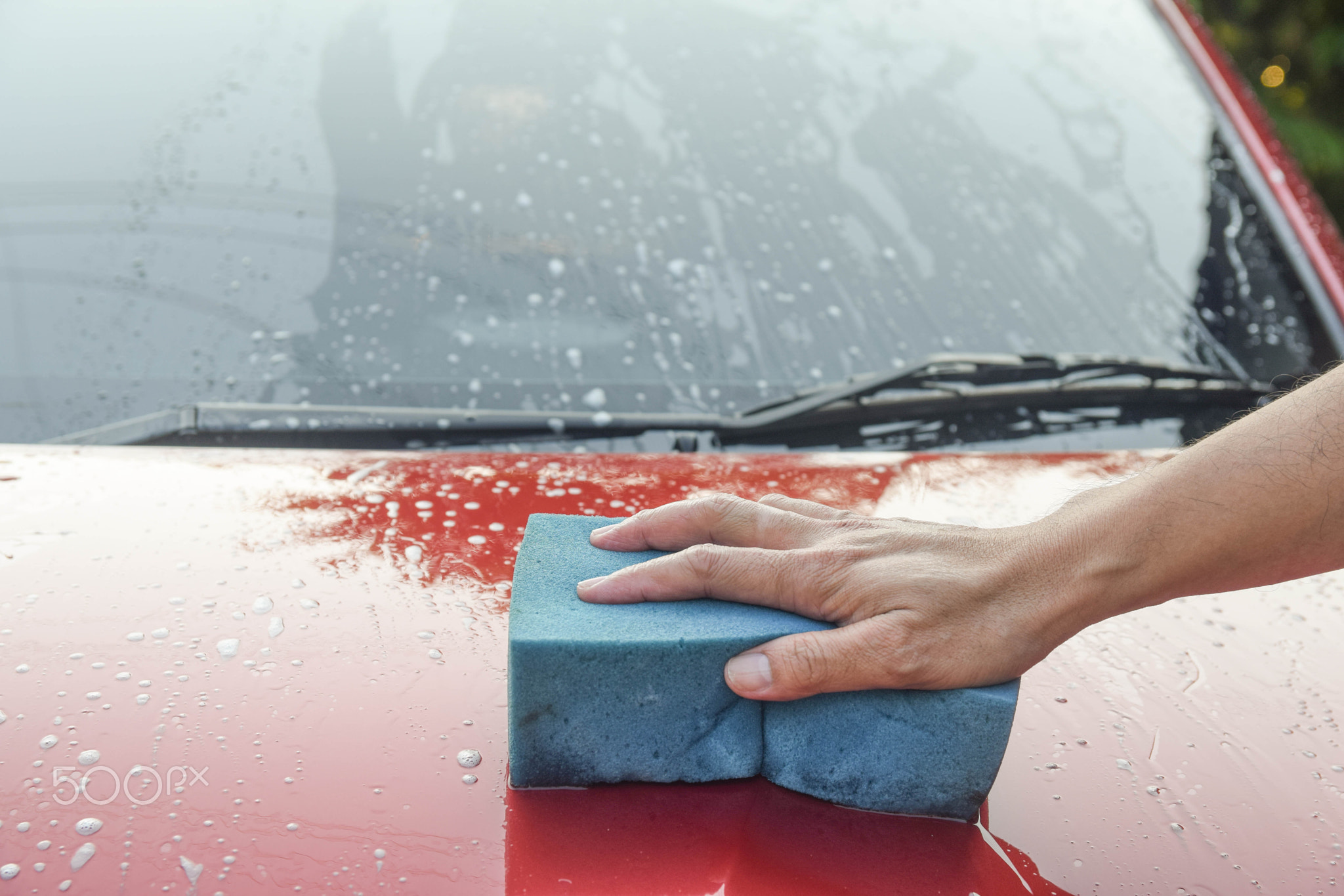 Man cleaning red automobile with blue sponge at car wash with