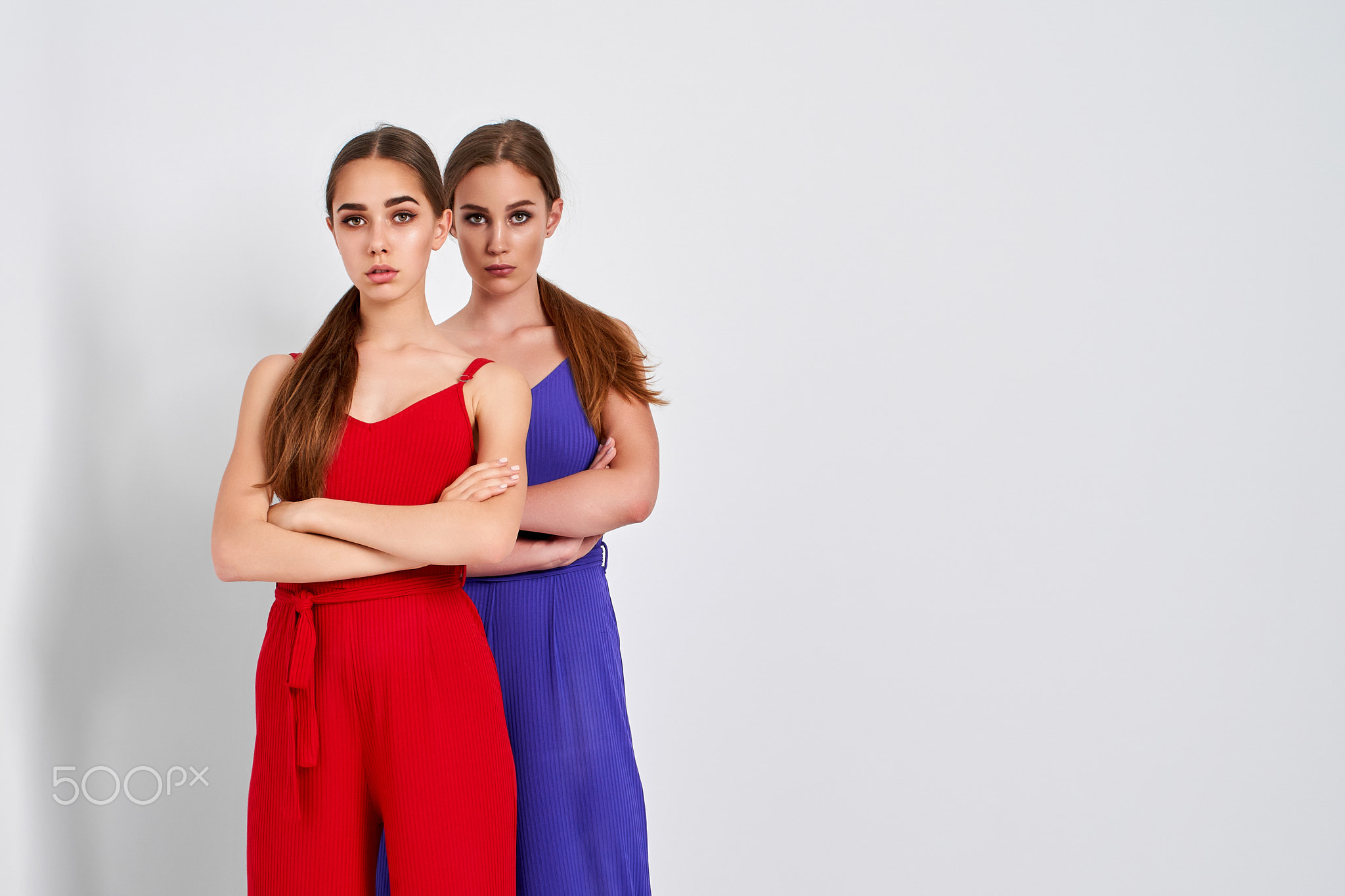 Two girls standing in studio in elegant colorful overalls on white