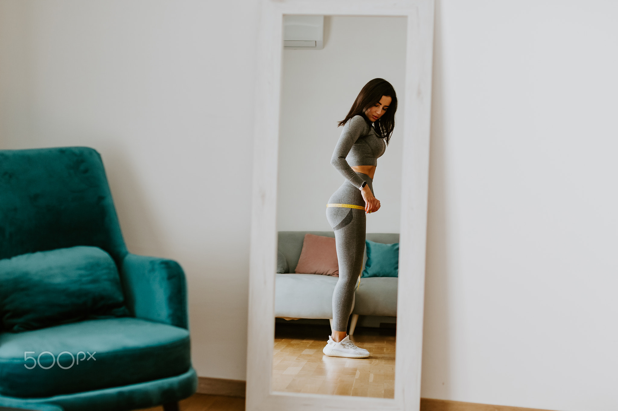 Fitness Woman Measuring body With Tape Standing In Front Of Mirror At