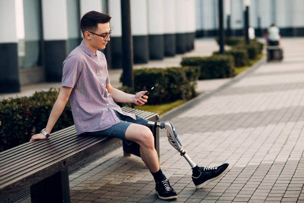 Disabled young man with foot prosthesis sitting on bench on city by Max Chernishev on 500px.com