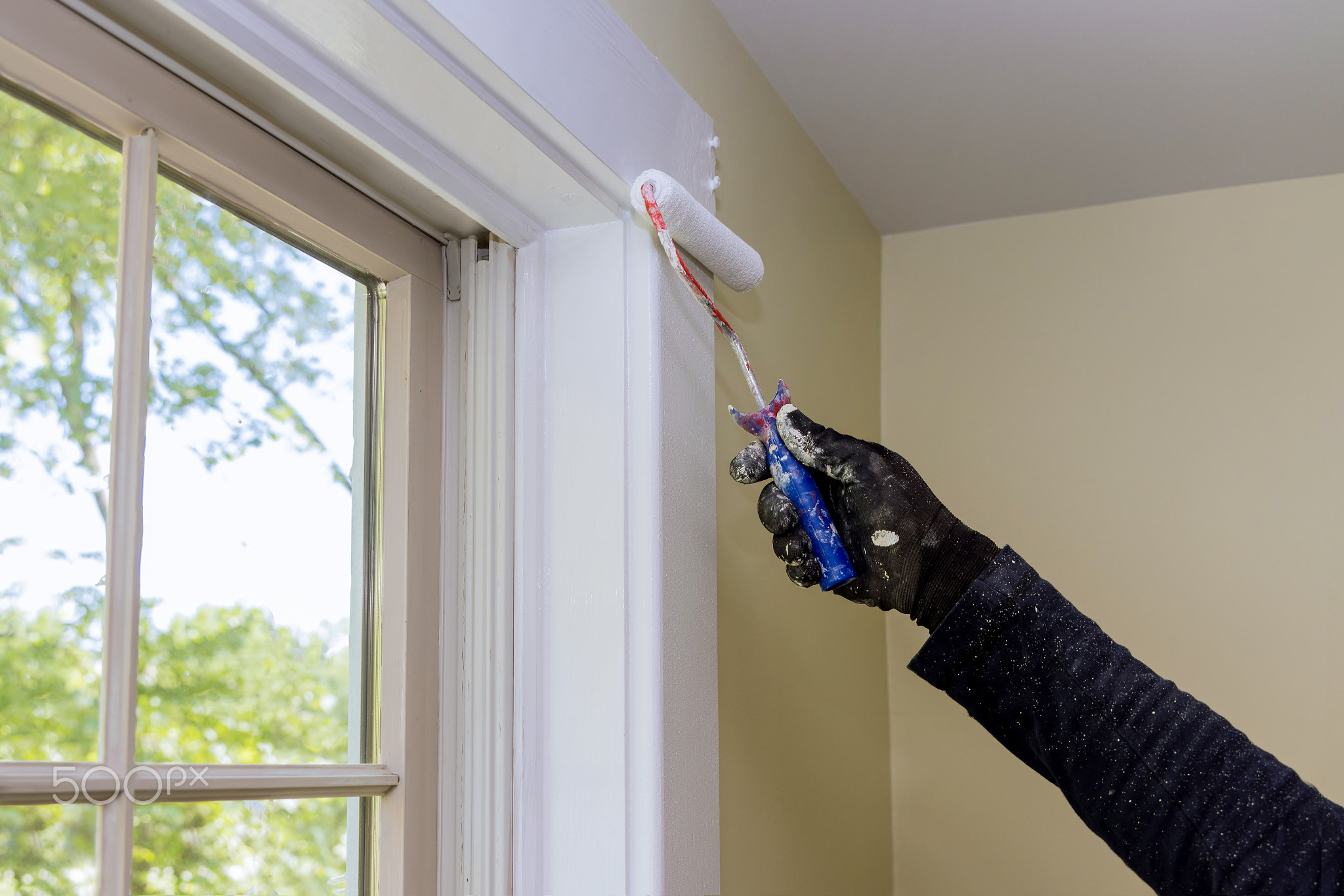 Worker painting using paint roller on layer white color a window frame