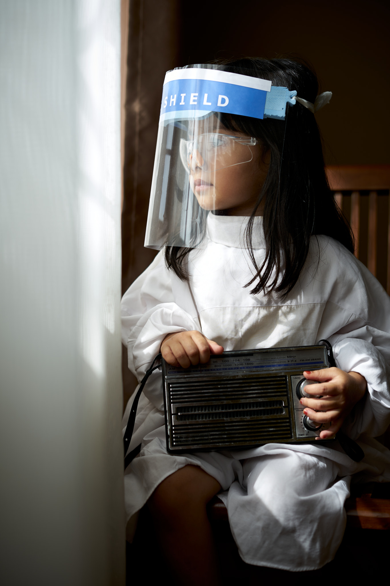 Little girl with face protective mask looking through the window