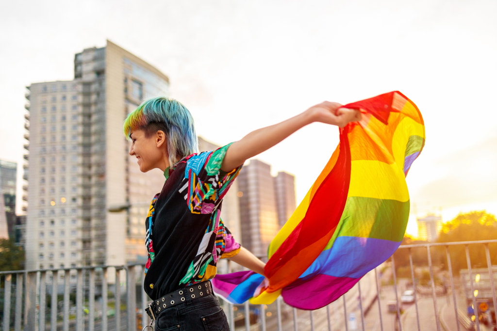 Portrait of happy non-binary person waving rainbow flag by Edyta Pawlowska on 500px.com