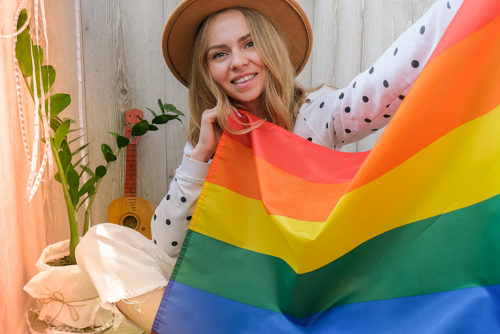 Young blonde woman with rainbow LGBTQ flag at home. Peace and freedom by Anastasiia Yanishevska on 500px.com