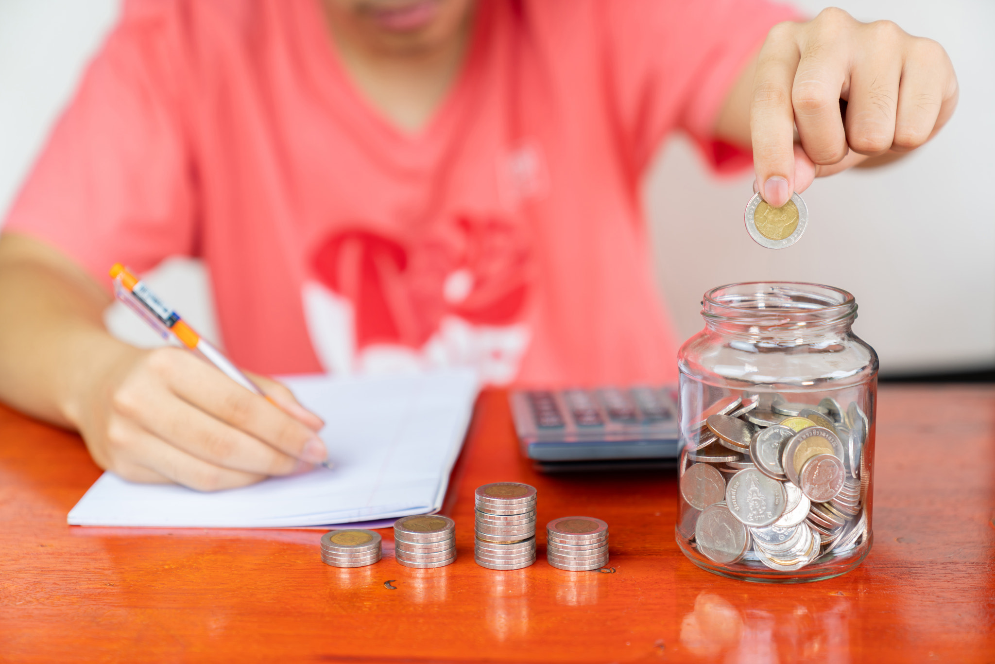 accounting put coin in glass bottle and calculator on wood table.