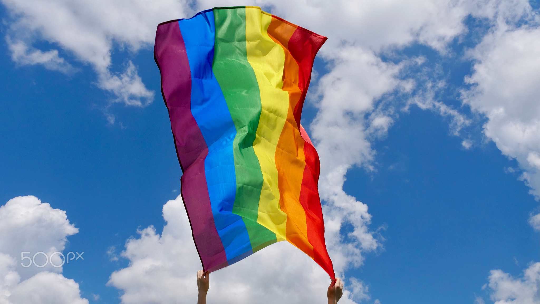 LGBT flag in hands on the background of the sky