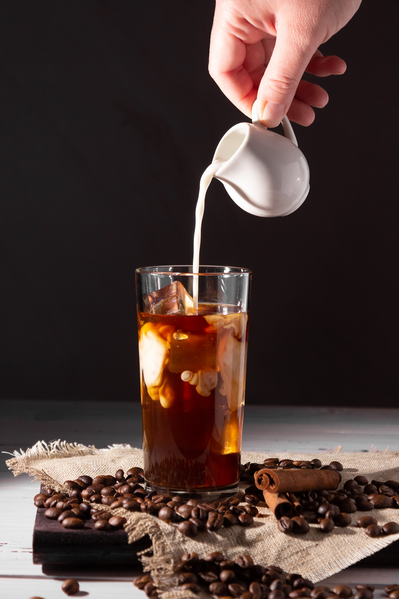 Glass cup with cold coffee and ice, coffee beans on a dark background.