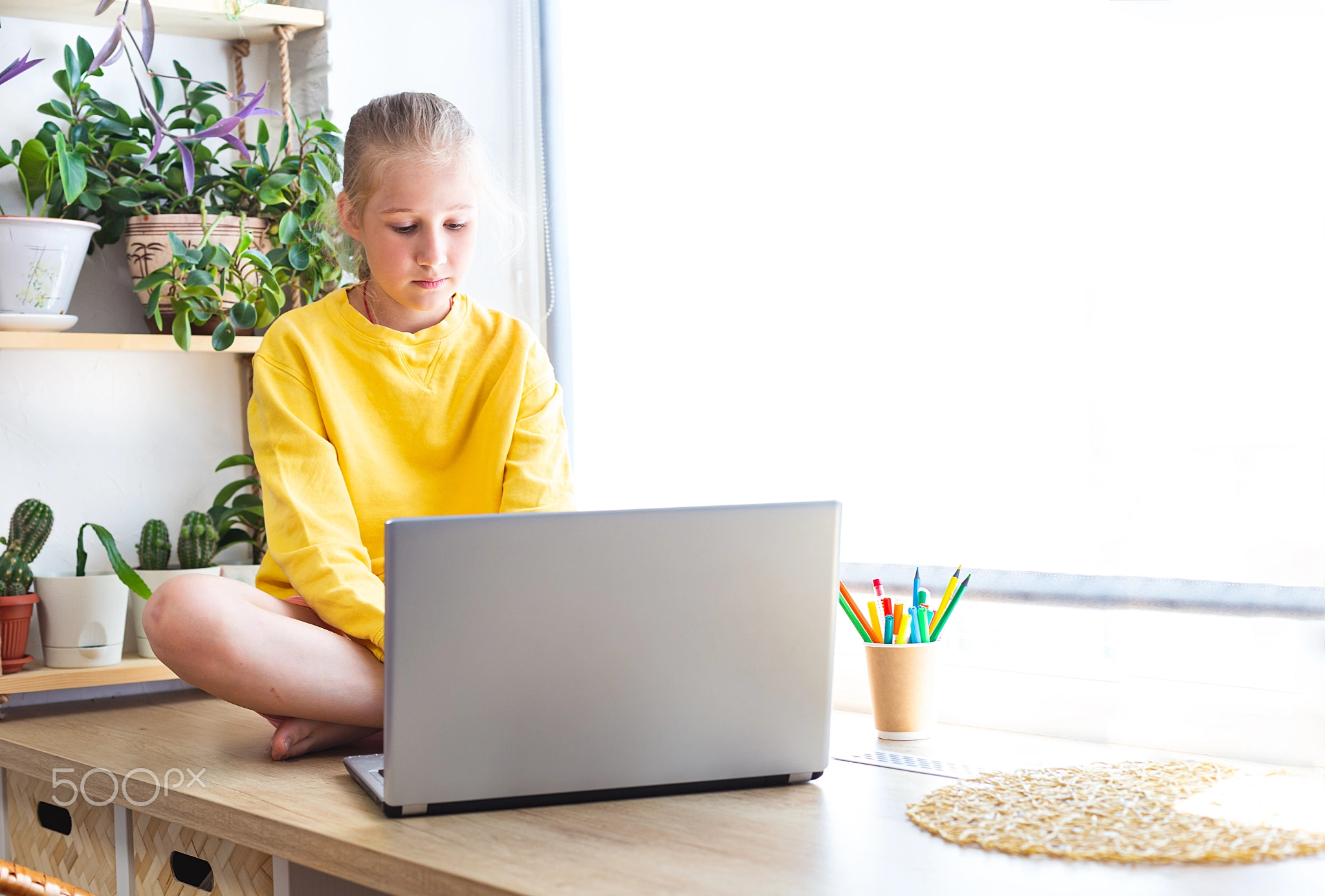 Caucasian girl sitting on the windowsill, near houseplants in front of