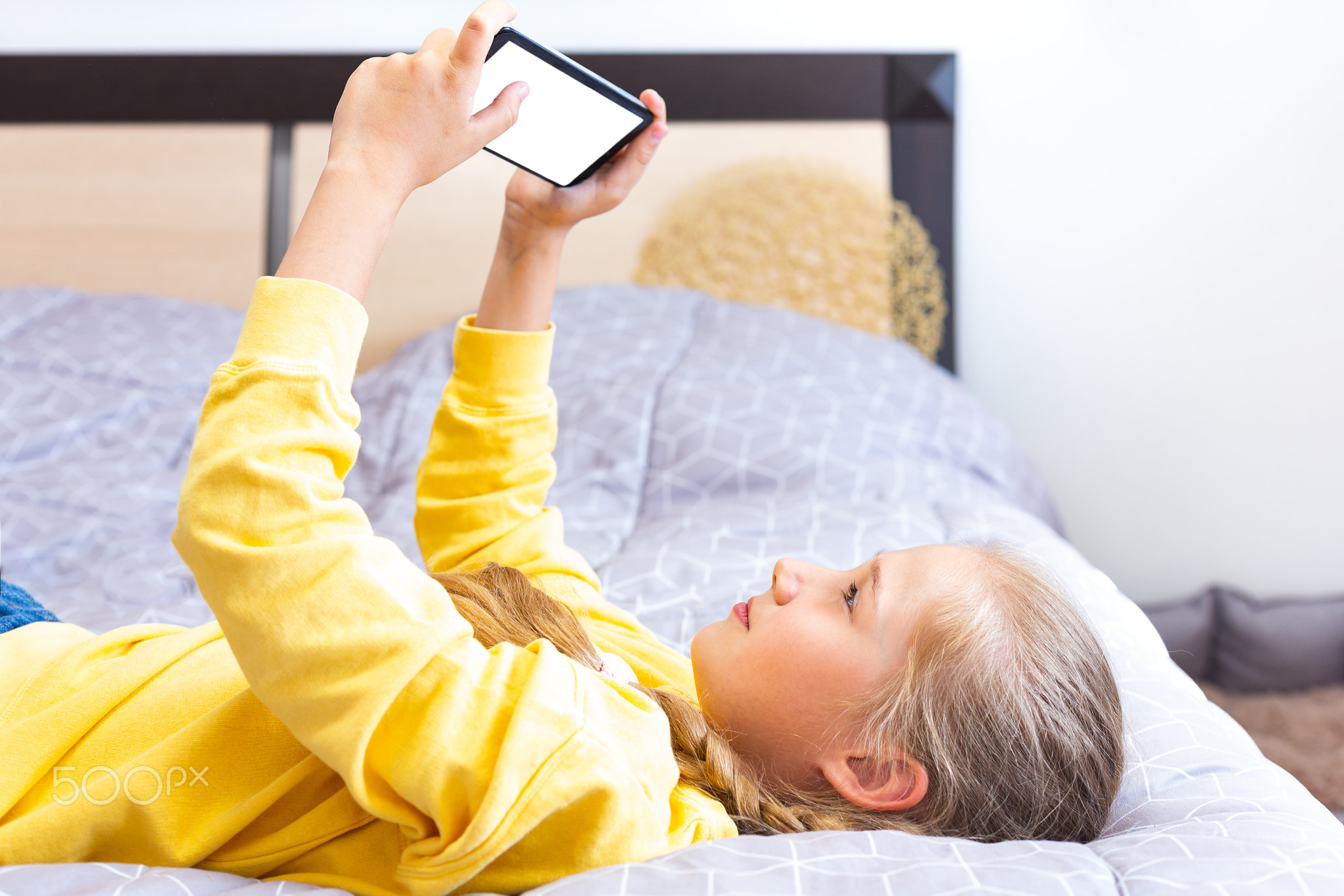 Teenage girl lying on the bed with a smartphone in her hands. White