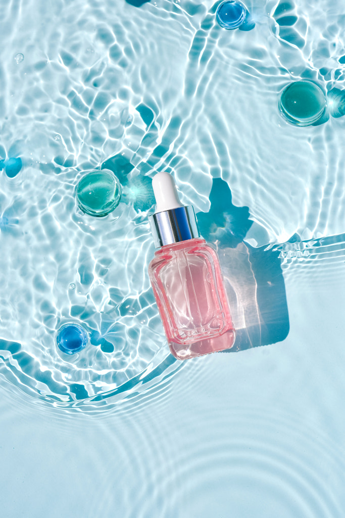 Cosmetic glass pink bottle with pipette and serum on water with waves by Irina Evva on 500px.com