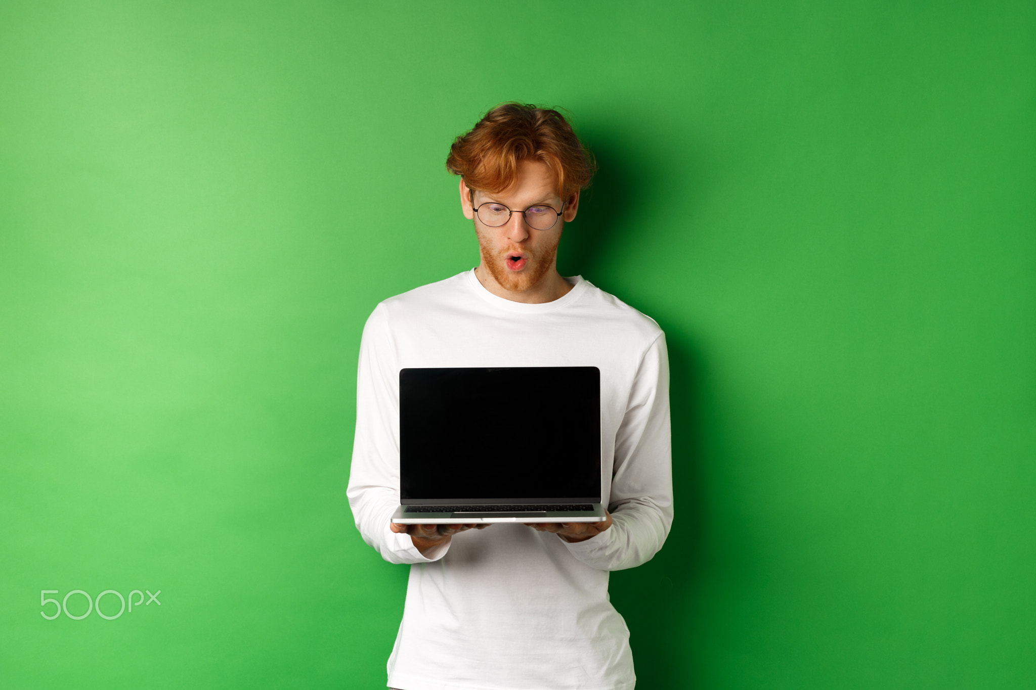 Impressed redhead nerdy guy in glasses showing blank laptop screen and
