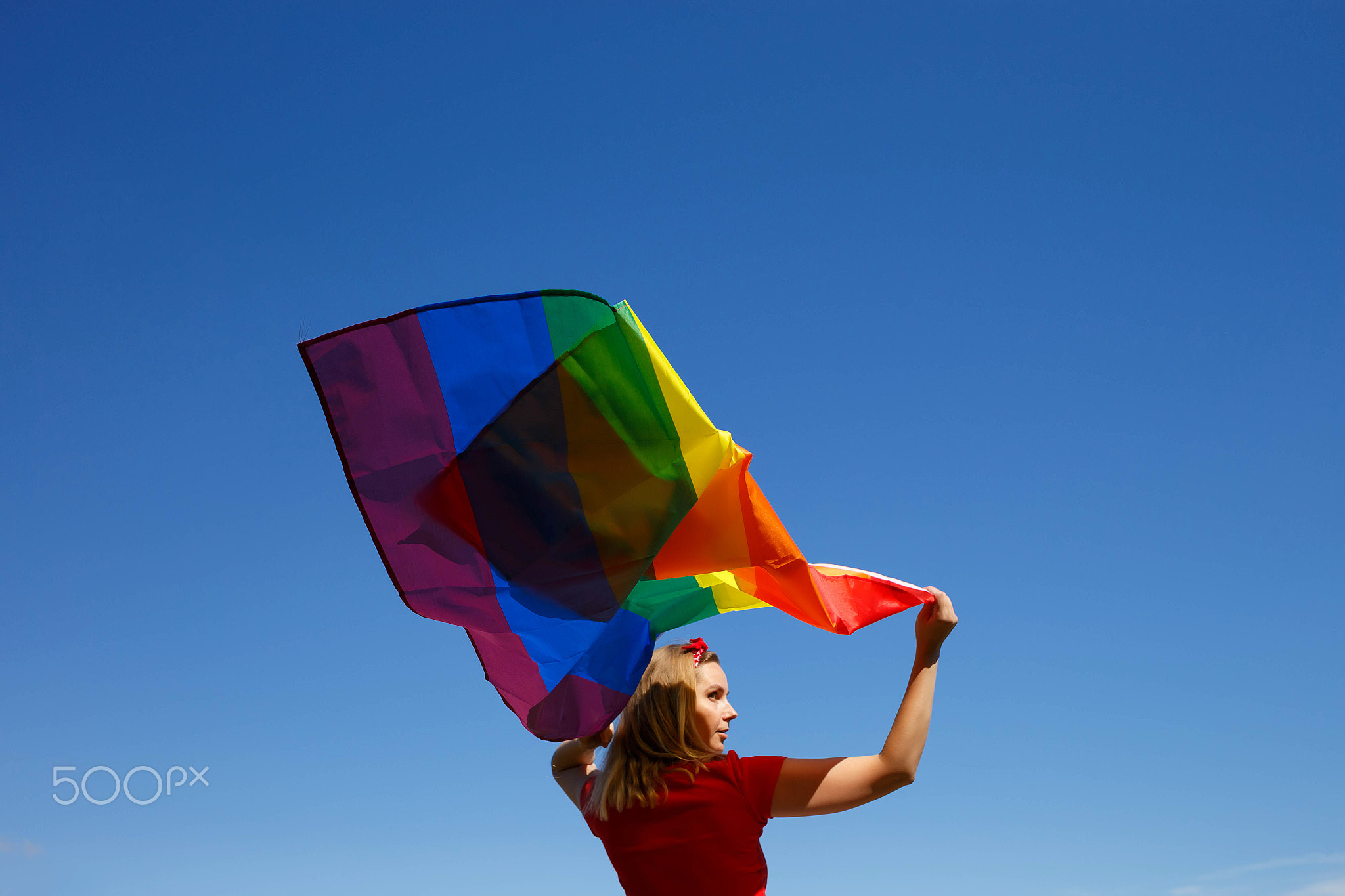 girl with lgbt flag behind her back against a bright blue sky