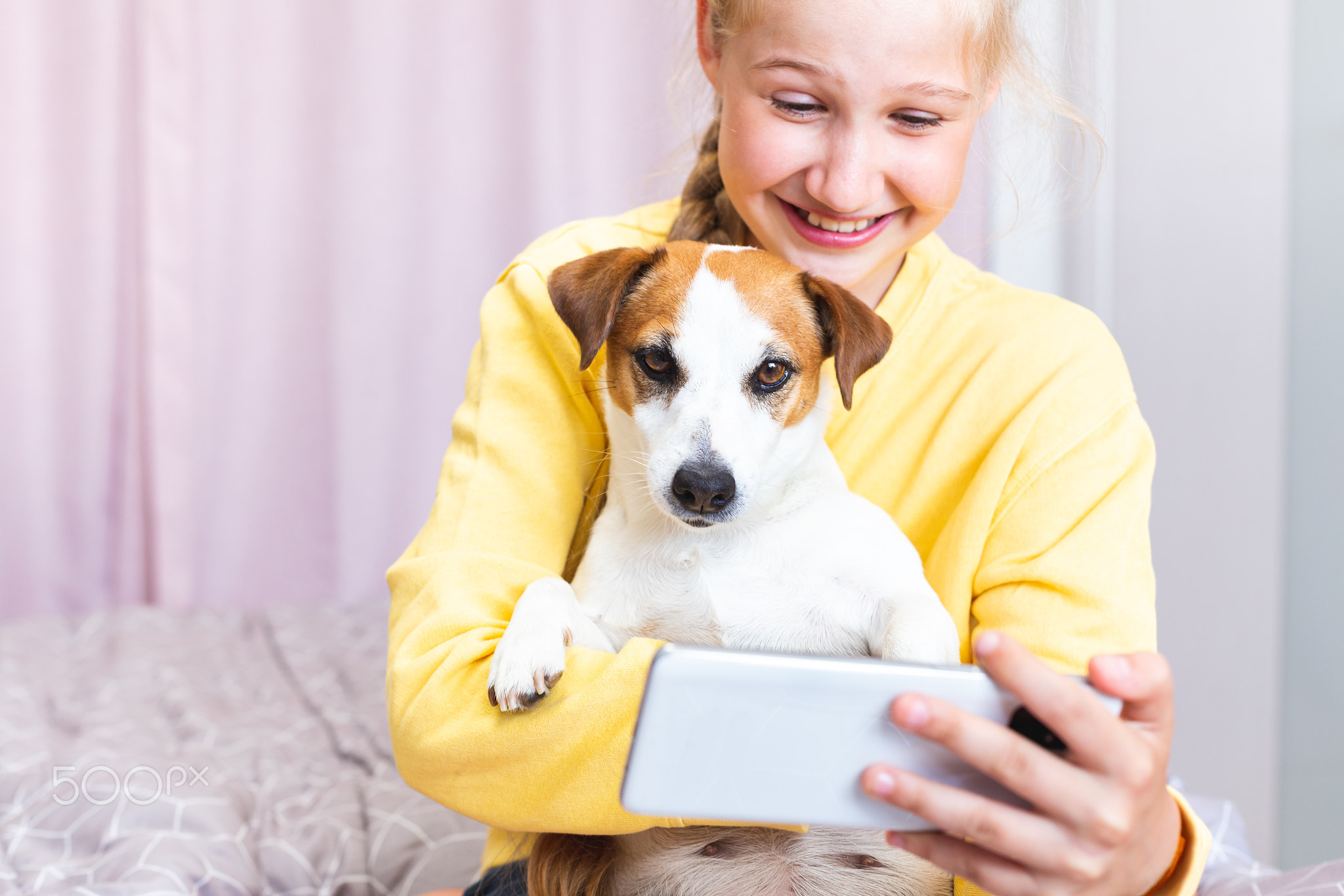 A laughing teenage girl with a dog andmobile phone in her hand. Close