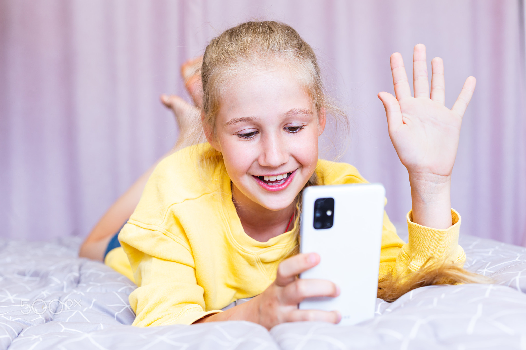 A Caucasian teenage girl with a phone in her hands, lying on the bed