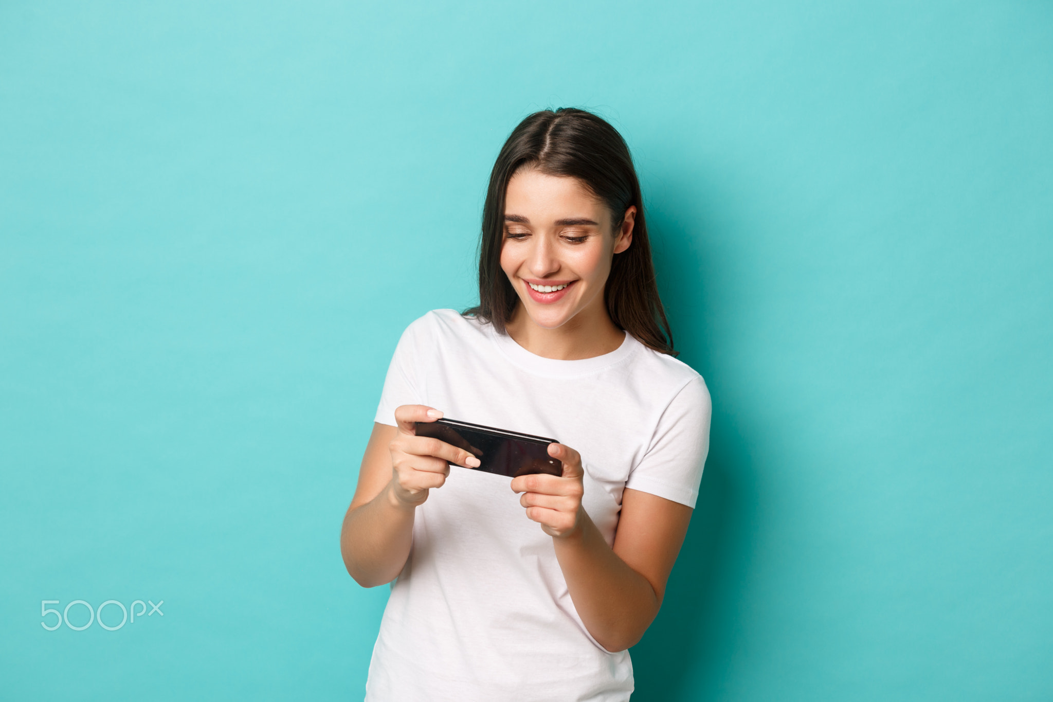 Image of happy young woman in white t-shirt, playing mobile phone game