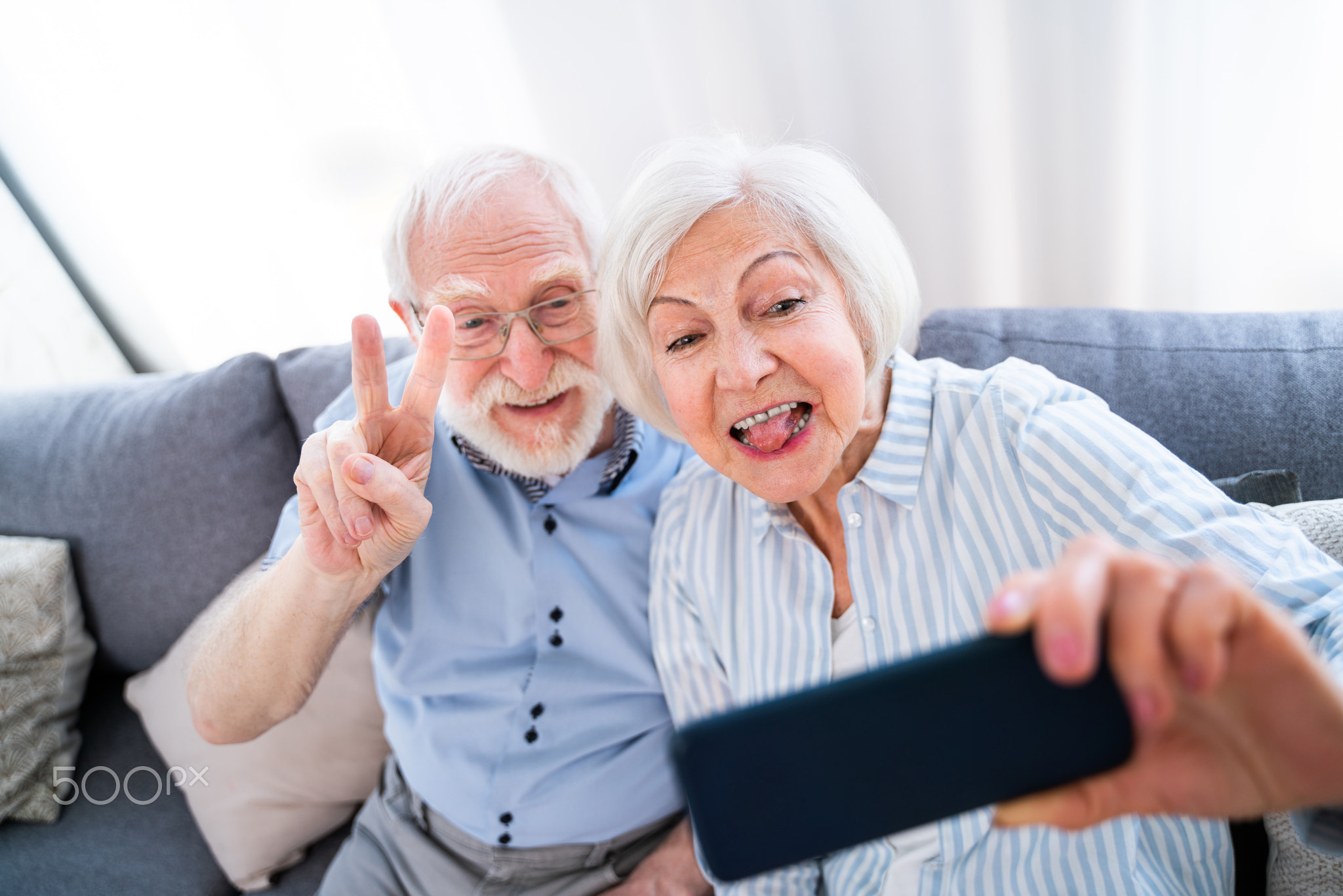 Cool elderly couple taking selfie with smartphone at home