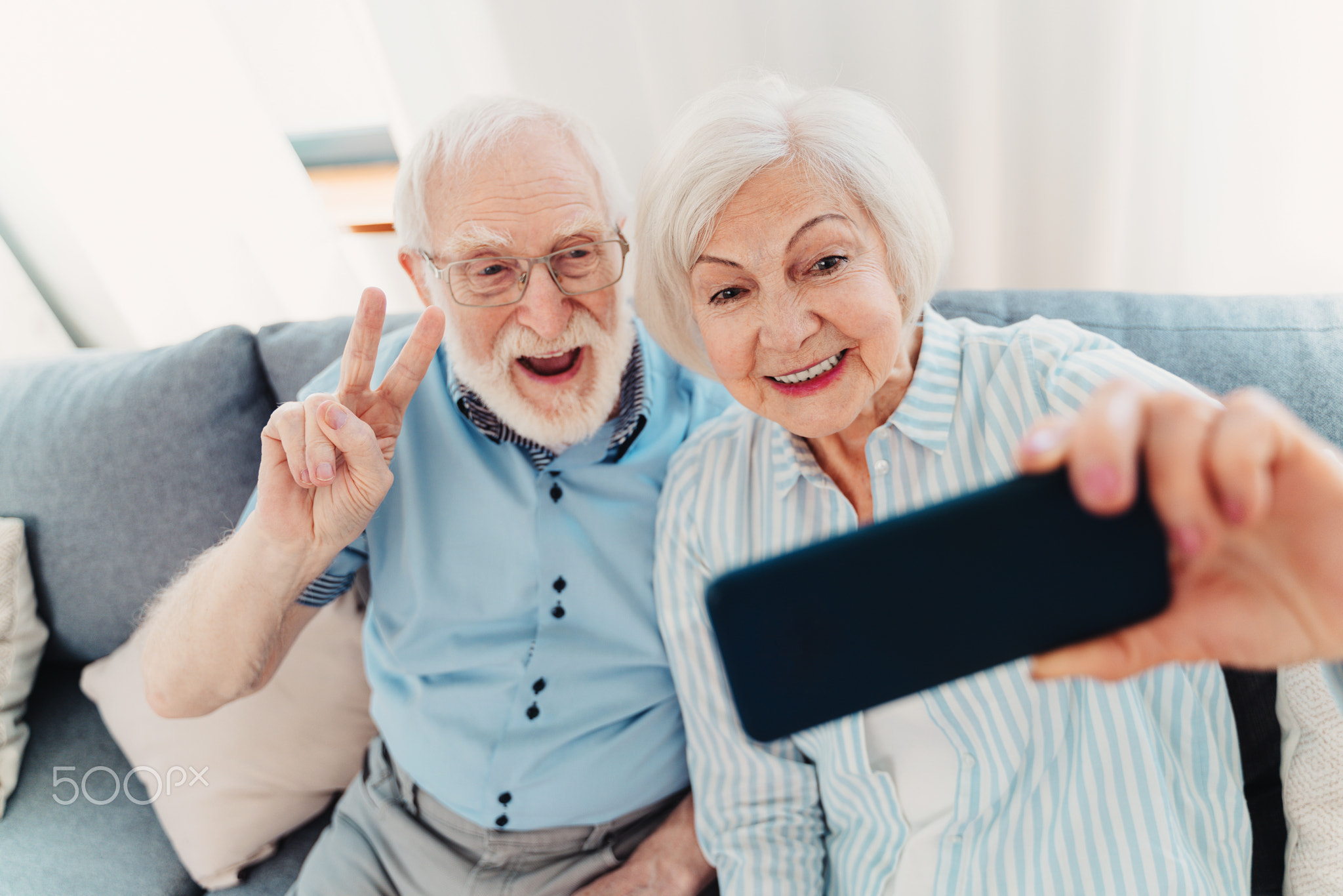 Cool elderly couple taking selfie with smartphone at home