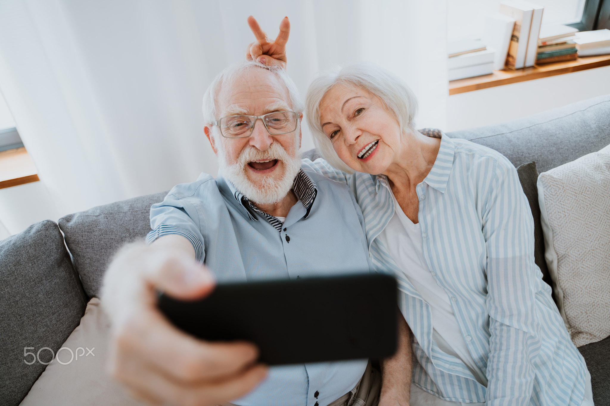 Cool elderly couple taking selfie with smartphone at home