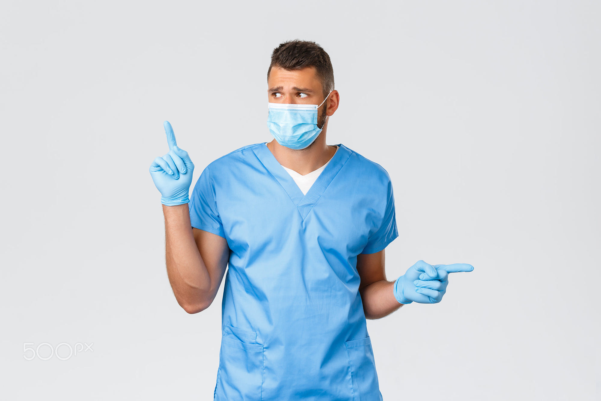 Healthcare workers, covid-19, coronavirus and preventing virus concept: Healthcare workers, covid-19, coronavirus and preventing virus concept. Concerned and distressed handsome doctor, nurse or intern in scrubs and medical mask, look left, pointing sideways.