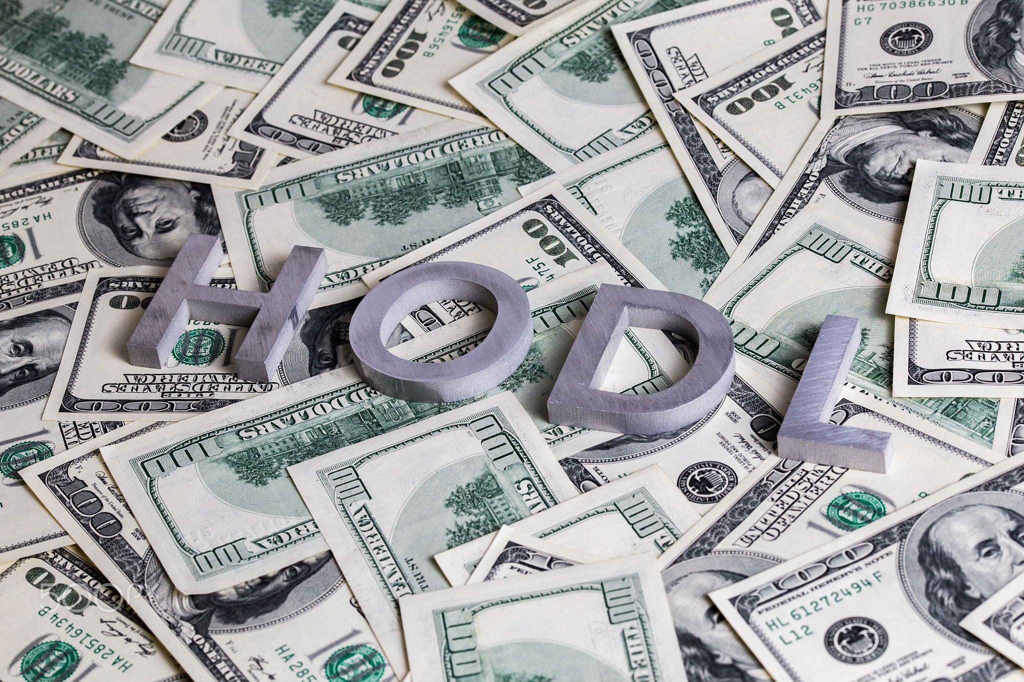The words HODL laid with aluminium letters on dollar banknotes - with