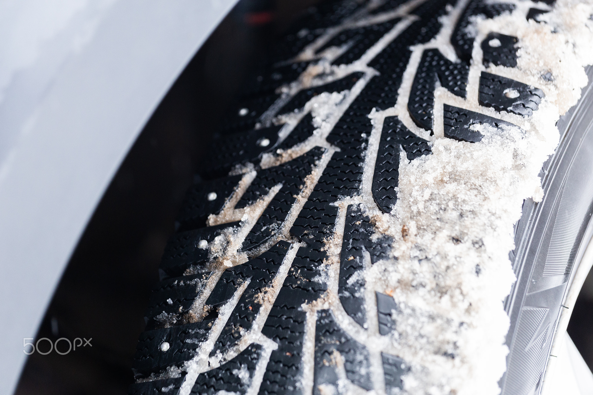 an unadorned picture of winter car wheel with metal spikes on snow