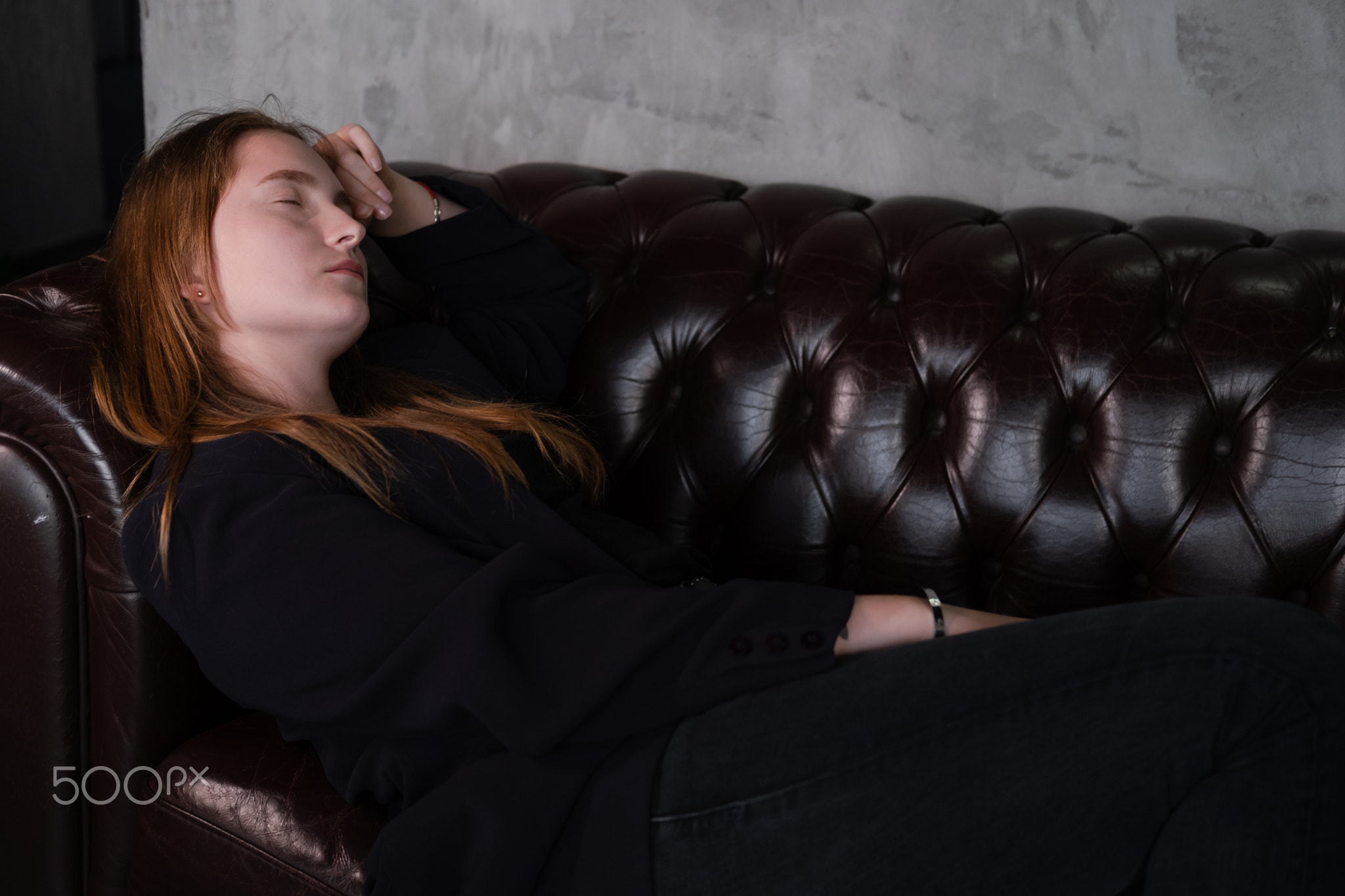 beautiful confident brunette woman in black on a brown leather couch