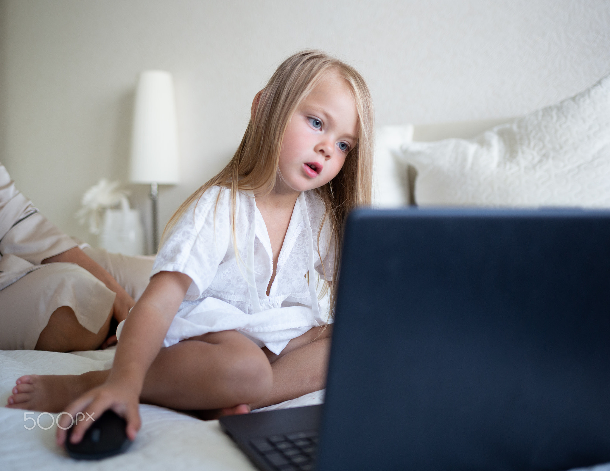 little cute girl sitting on the bed in front of a laptop