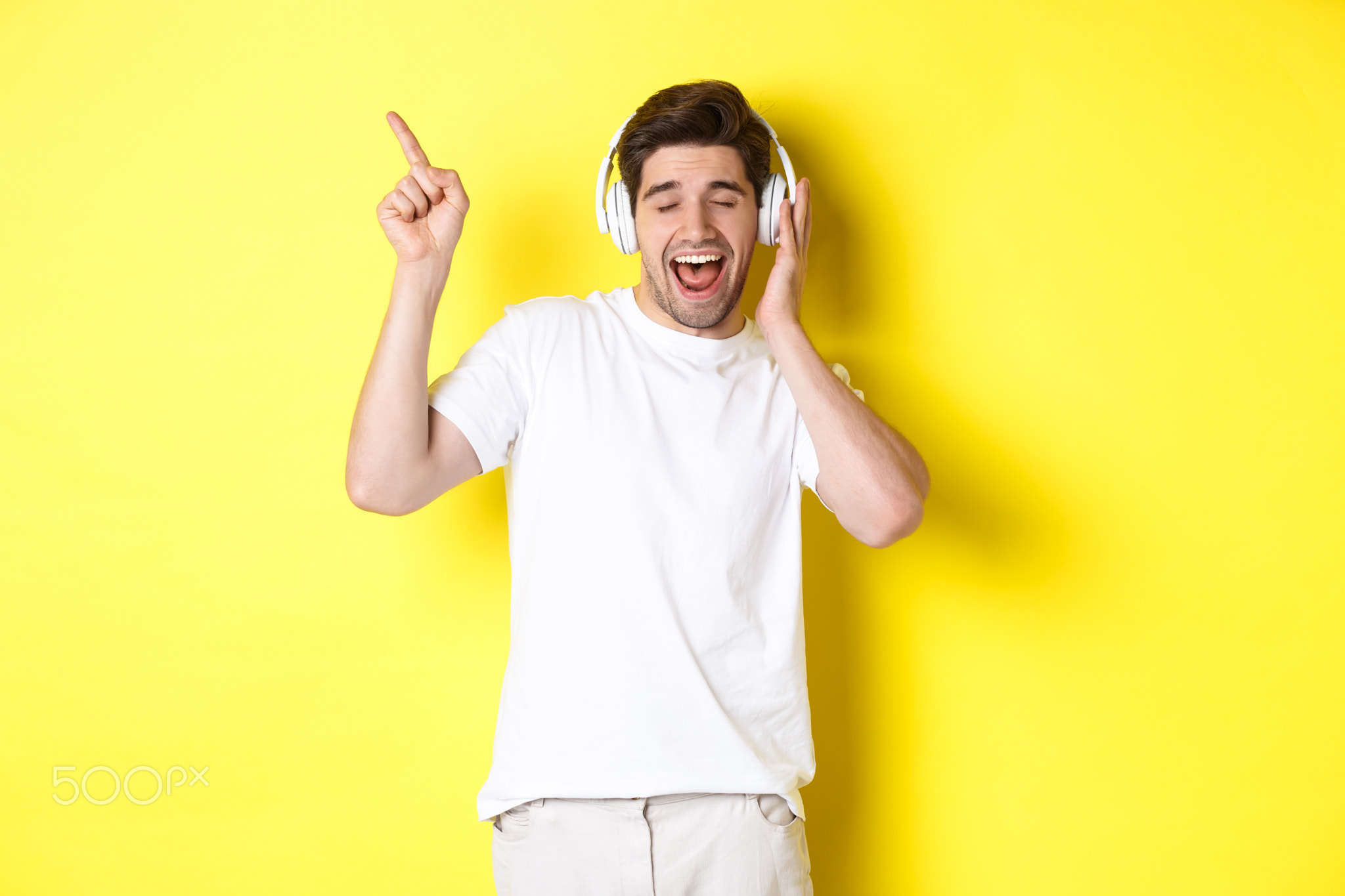 Happy man listening music in headphones, pointing finger at promo