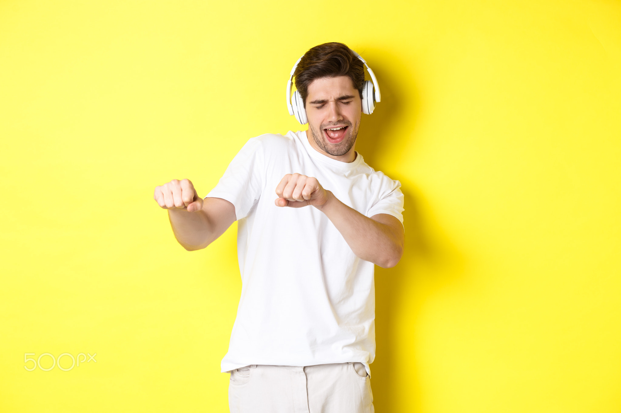 Cool guy listening music in headphones and dancing, standing in white