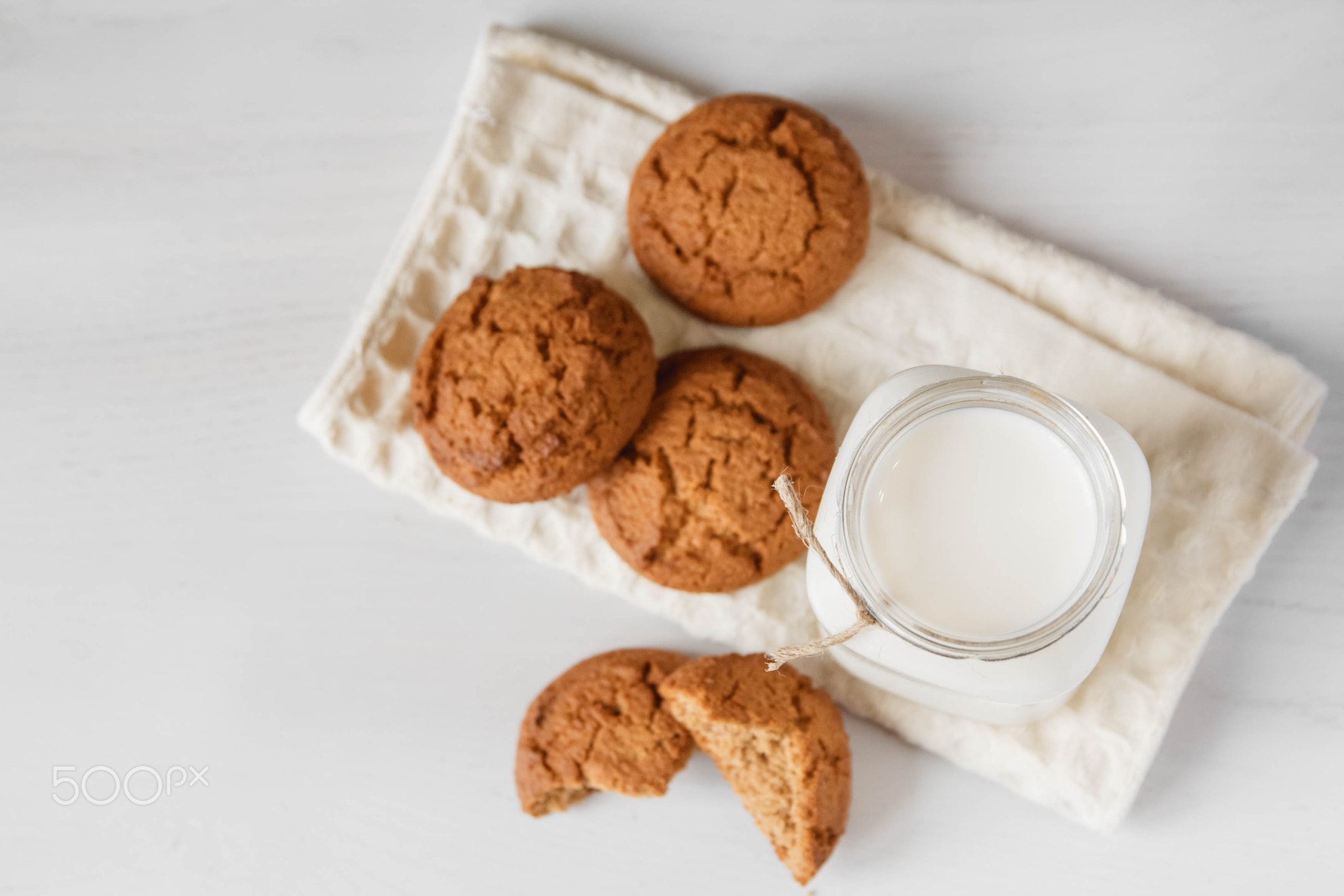 Milk in glass jar and oatmeal cookies near napkin on white table