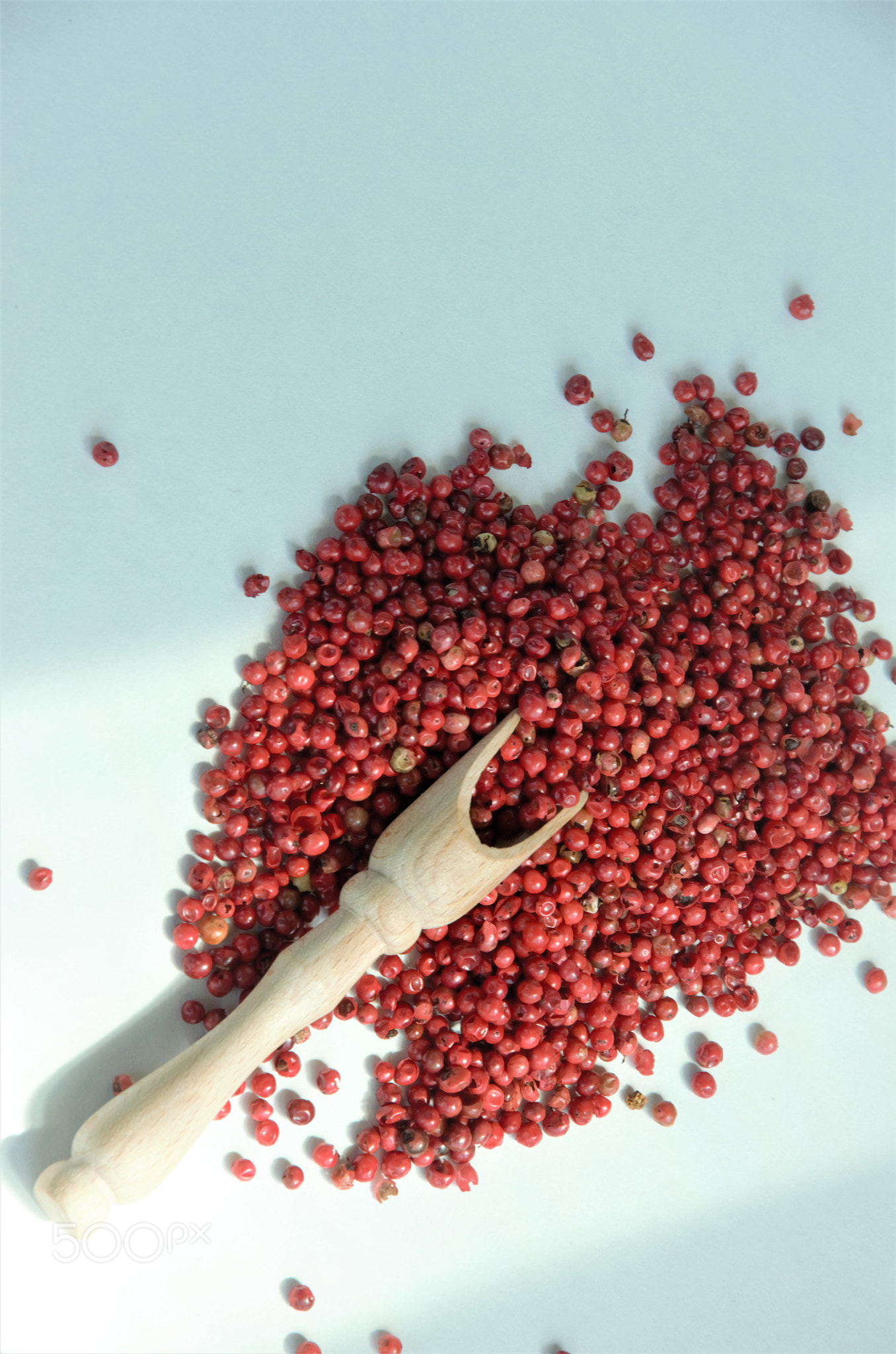 pink pepper with a wooden spoon on a white background