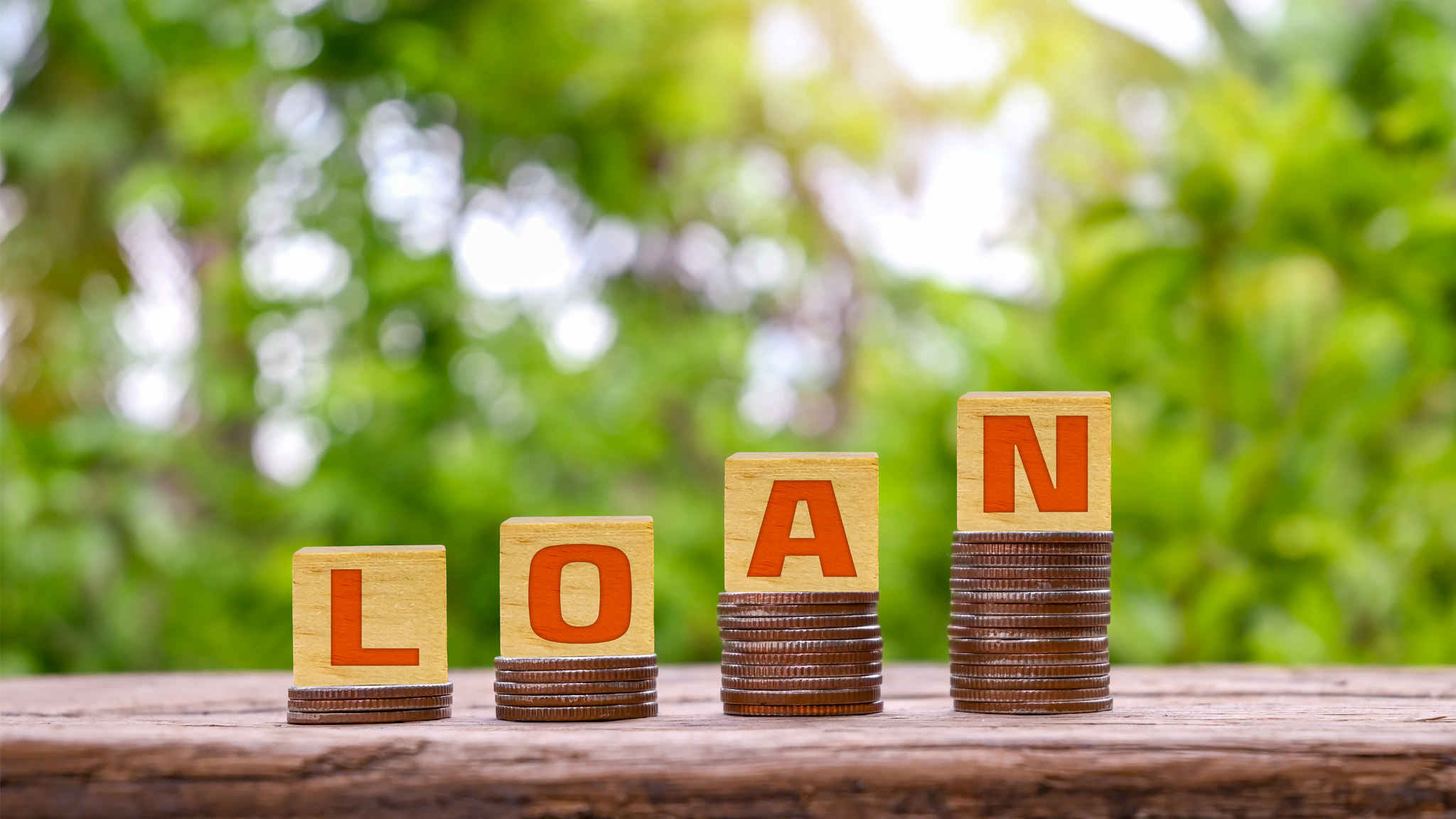 Wooden block with loan text on pile of coins