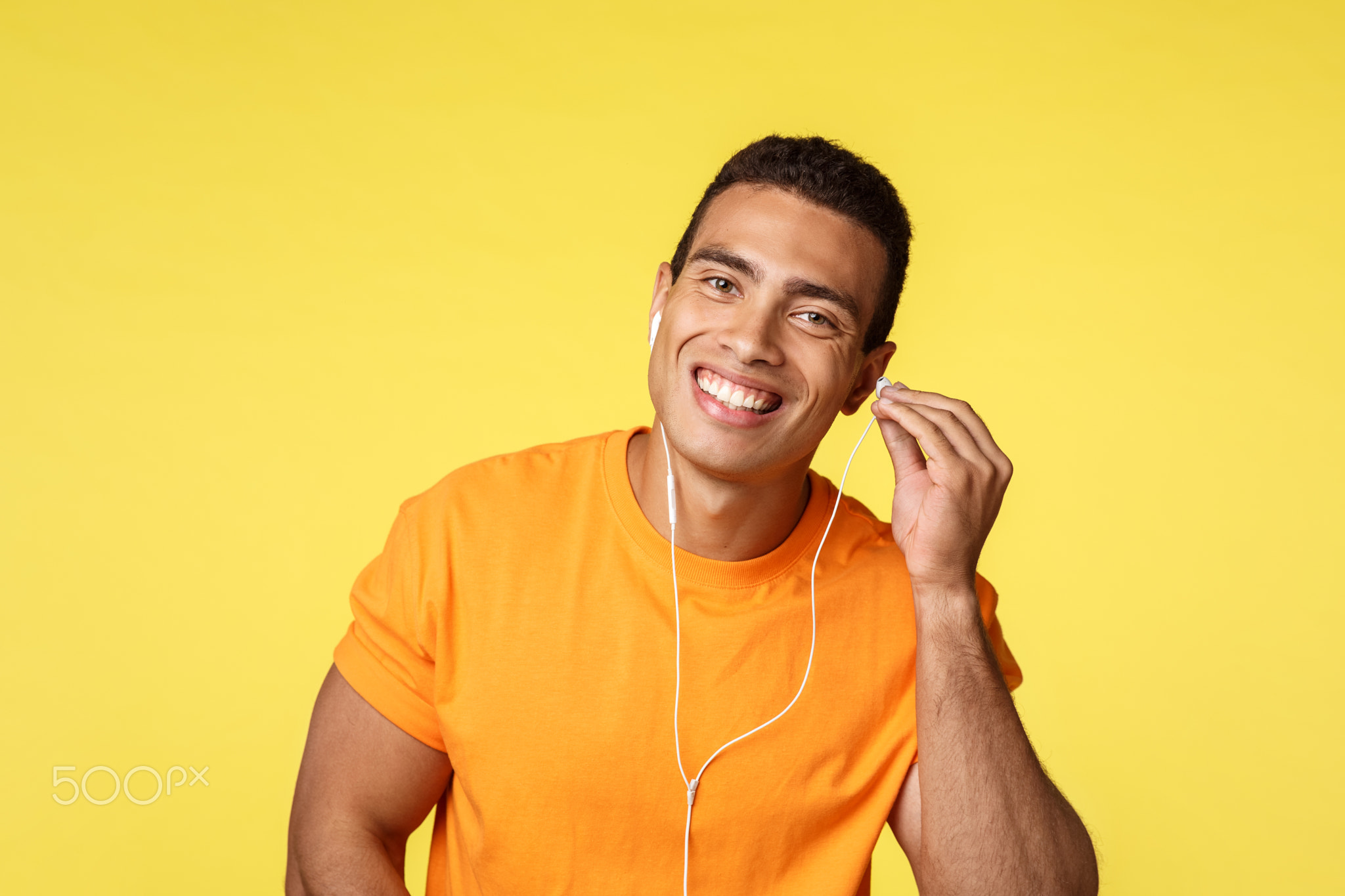 Cheerful handsome male athlete in orange t-shirt place headphone in