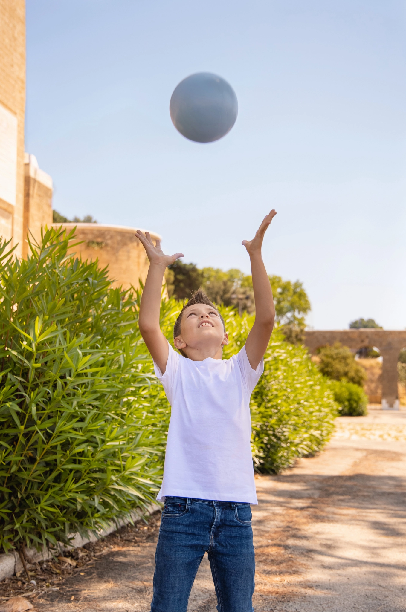 Happy kid boy in white t-shirt playing ball outdoors. Shirt mockup