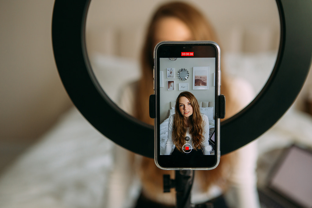 une jeune femme enregistre une vidéo sur un téléphone, un téléphone sur un trépied avec une lampe à led par Alena Spasskaya sur 500px.com