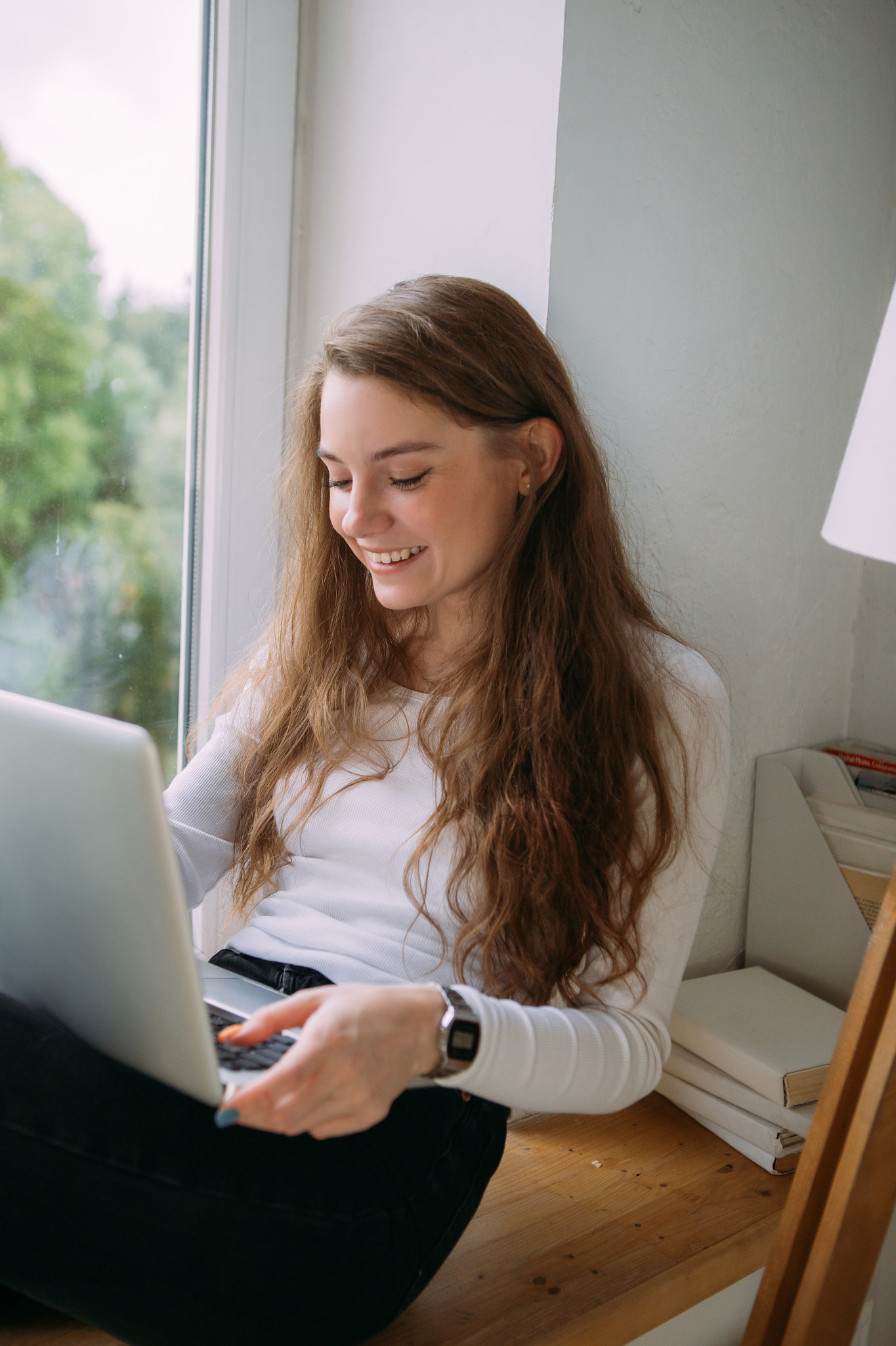 young girl working on laptop while sitting on the windowsill