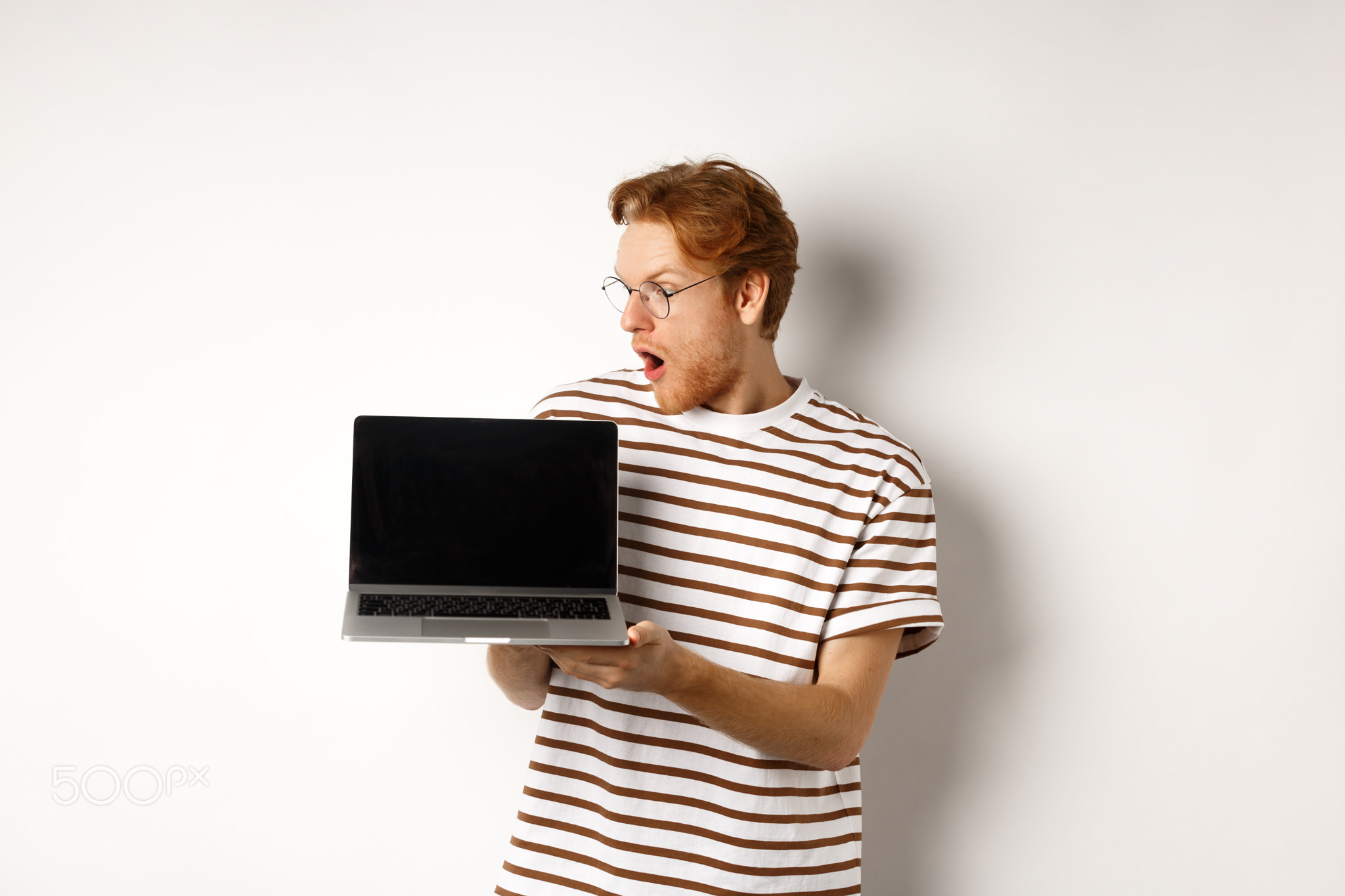Young redhead man look impressed, showing laptop empty screen with