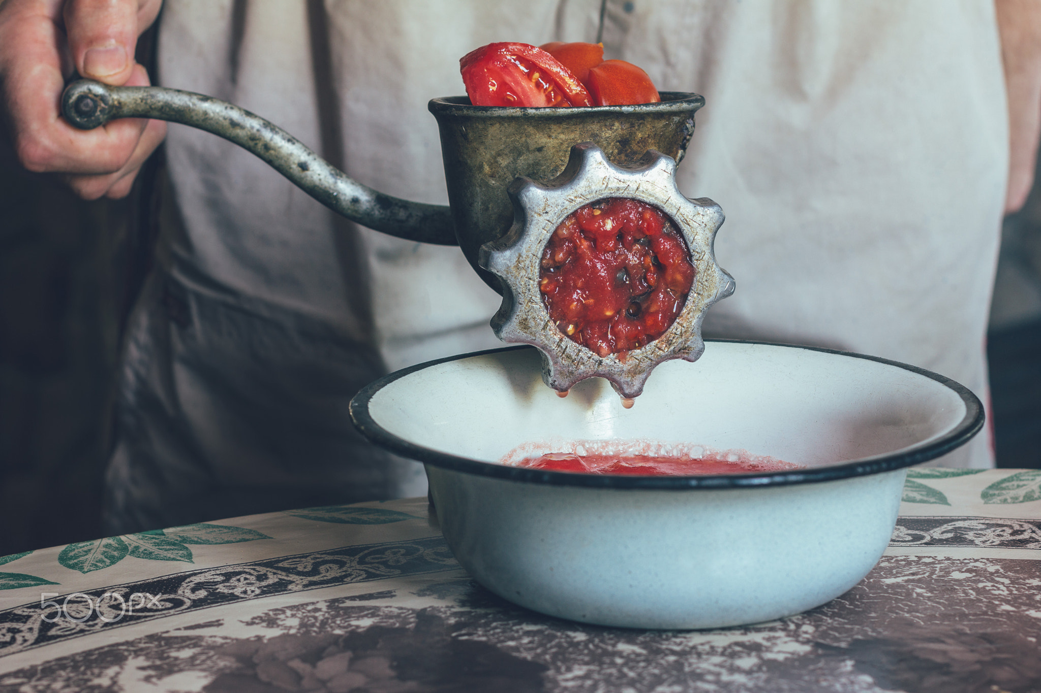 man with an old meat grinder makes tomato puree