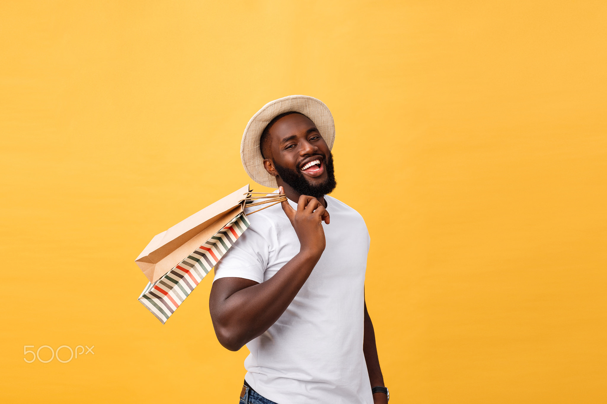 Happy african american man holding shopping bags on yellow background