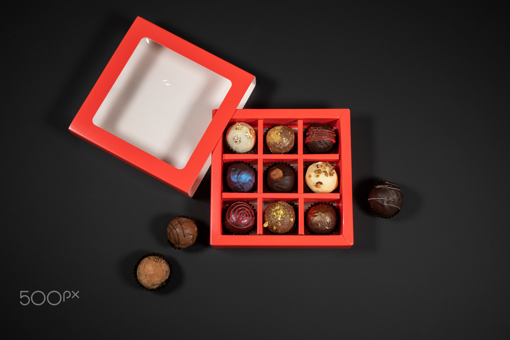 Various handmade chocolate truffle candies in a red box on a dark