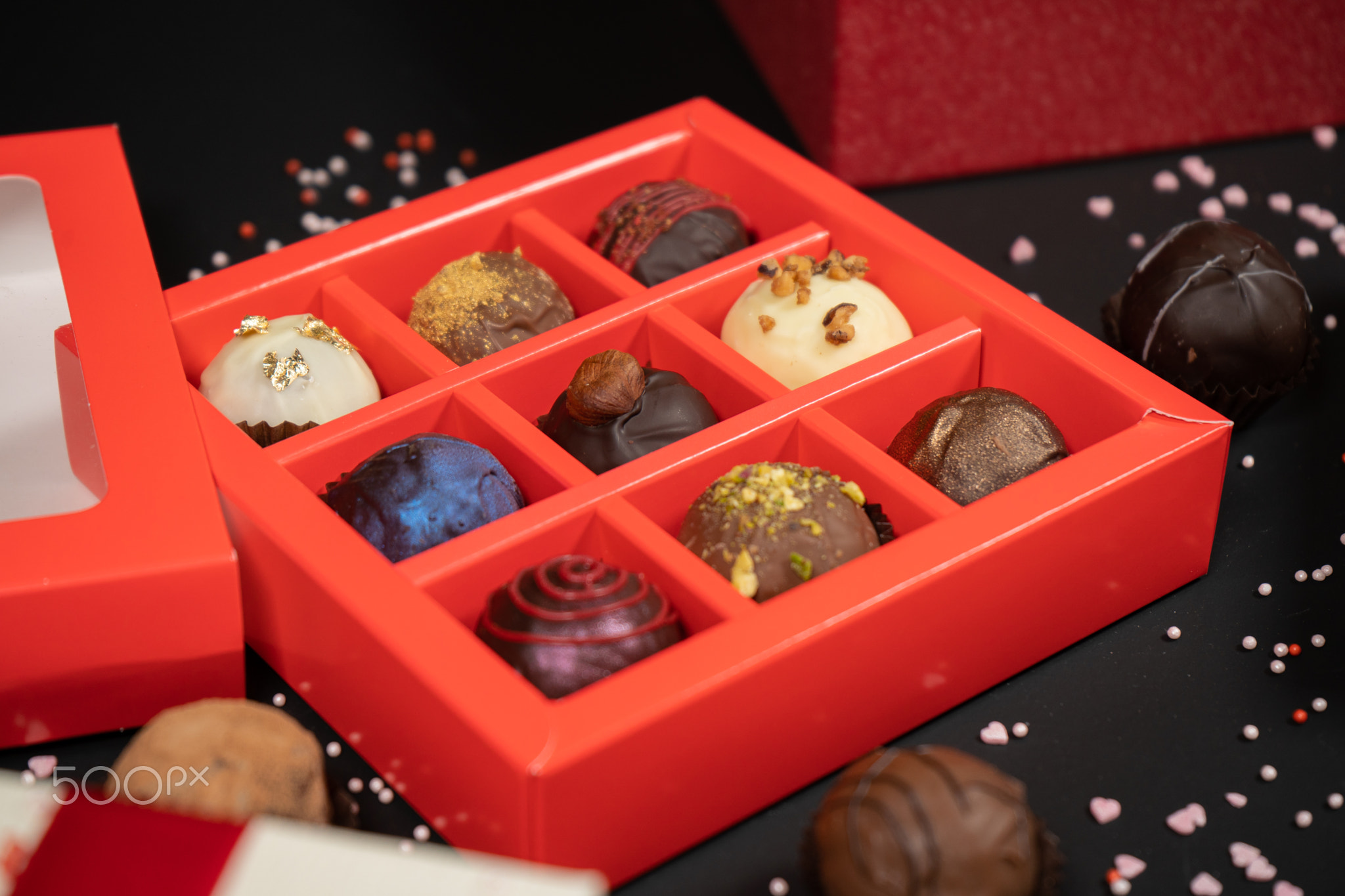 Various handmade chocolate truffle candies in a red box on a dark