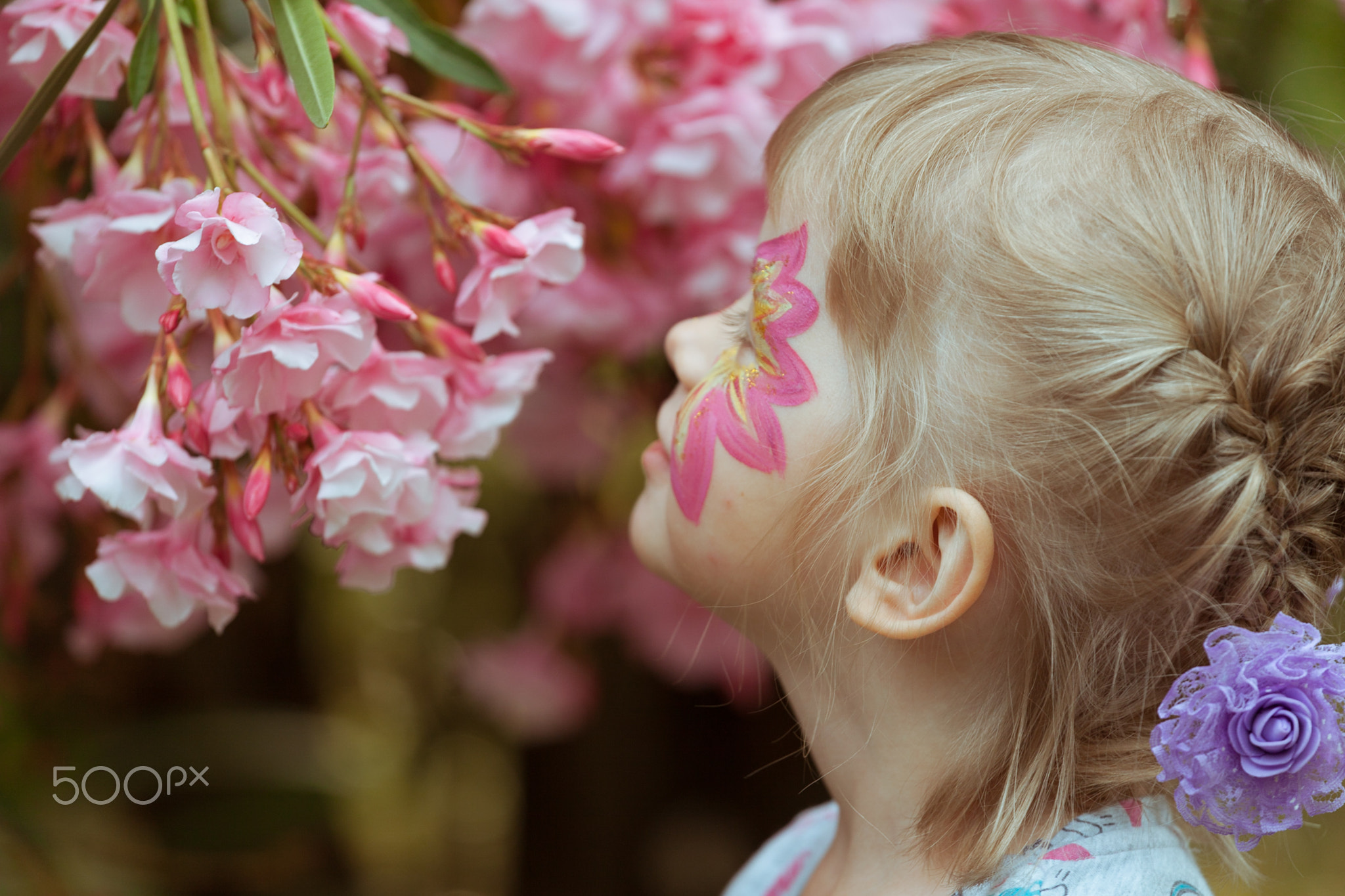 A girl with makeup on her face is sniffing pink flowers.
