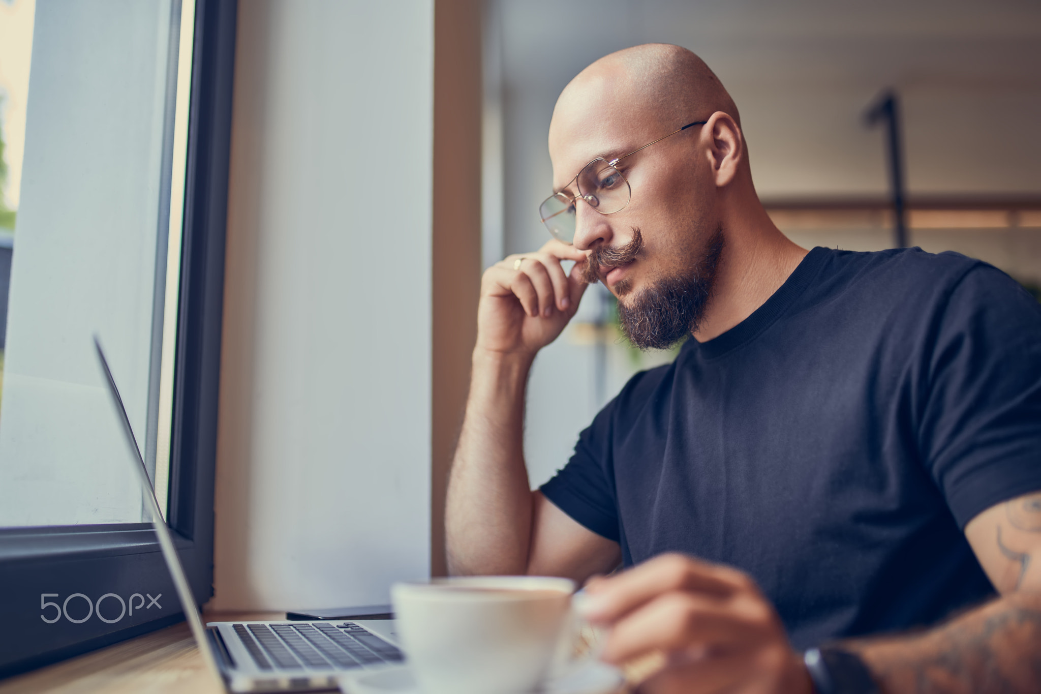 Focused hipster millennial man works at laptop while sitting in cafe