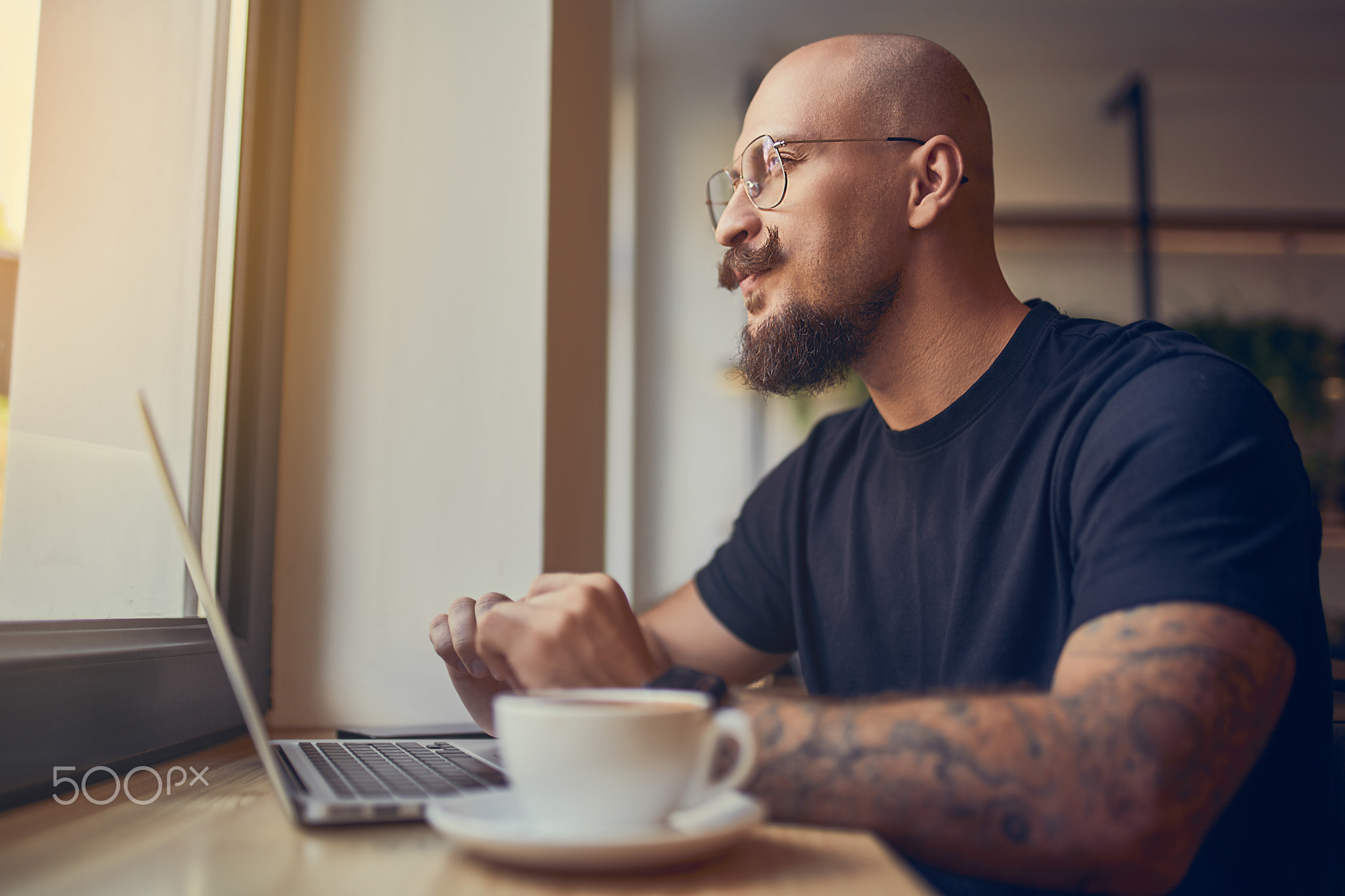 Focused hipster millennial man works at laptop while sitting in cafe
