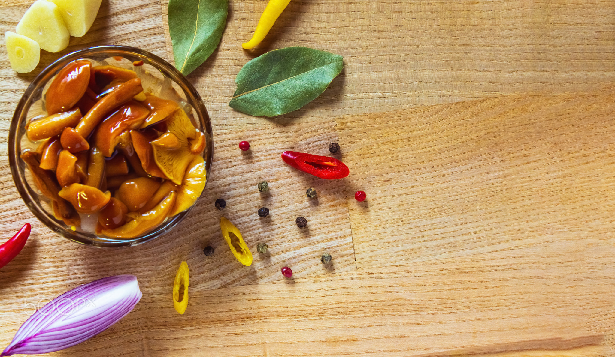 The pickled mushrooms stand on a wooden cutting board in a small glass