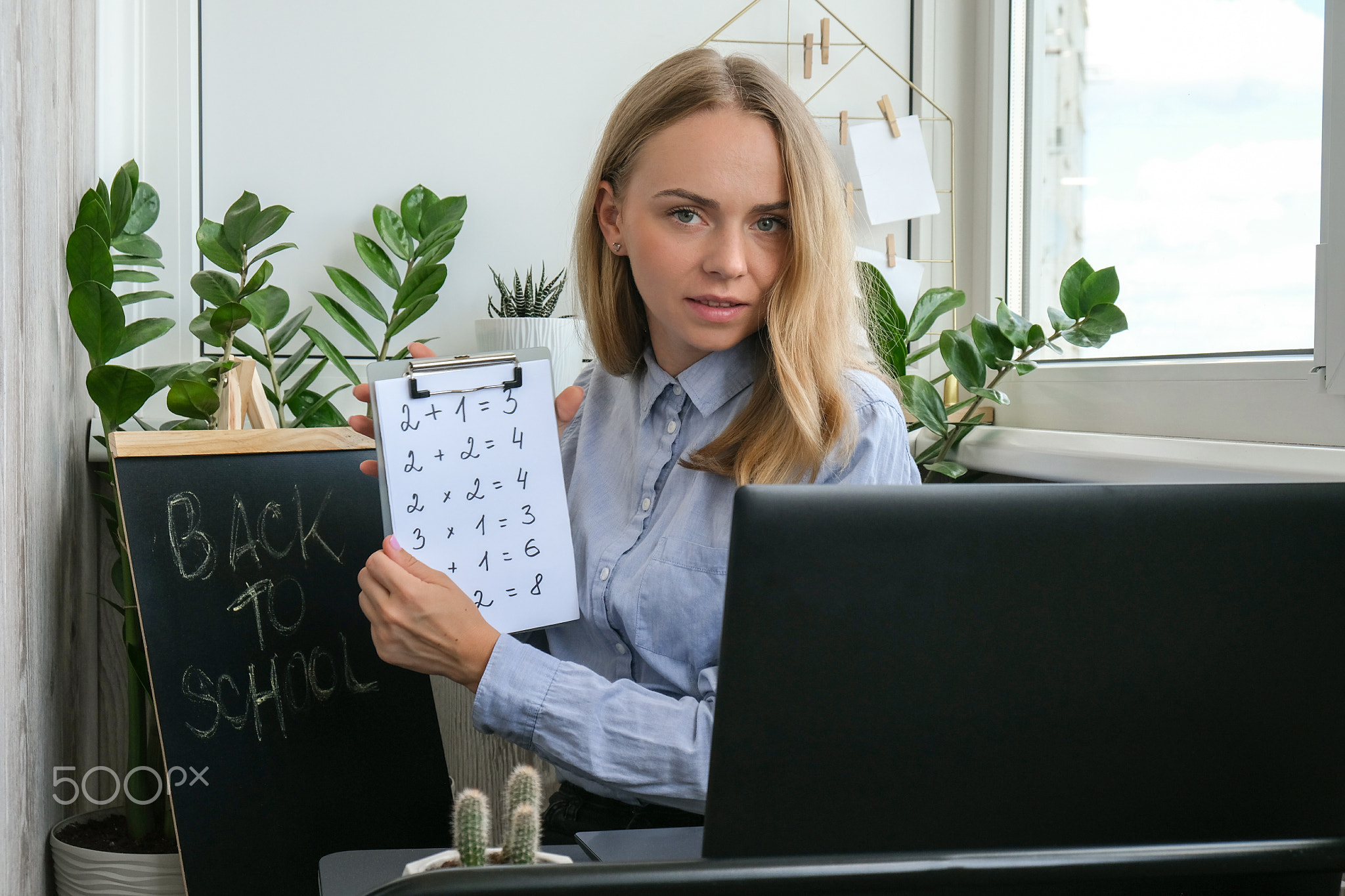 Young female teacher sitting at desk and using laptop teaching